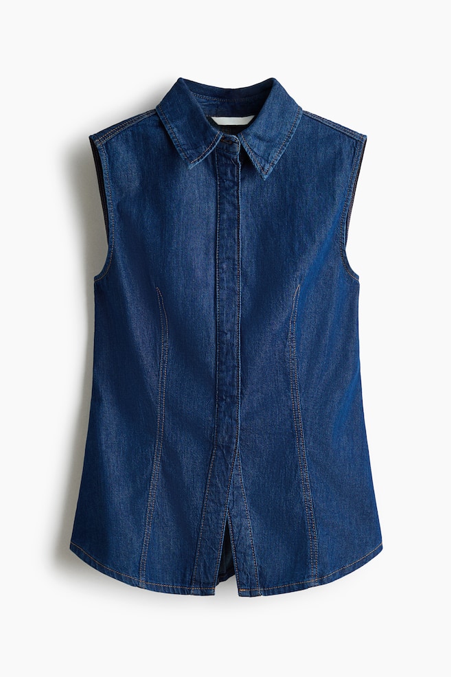 A dark blue denim sleeveless shirt is presenting its front, featuring a pointed collar and a button-front placket. It is showing visible tan contrast stitching along the seams, armholes, and collar, along with vertical shaping seams on the front, and a curved hem with a small front vent. - 1