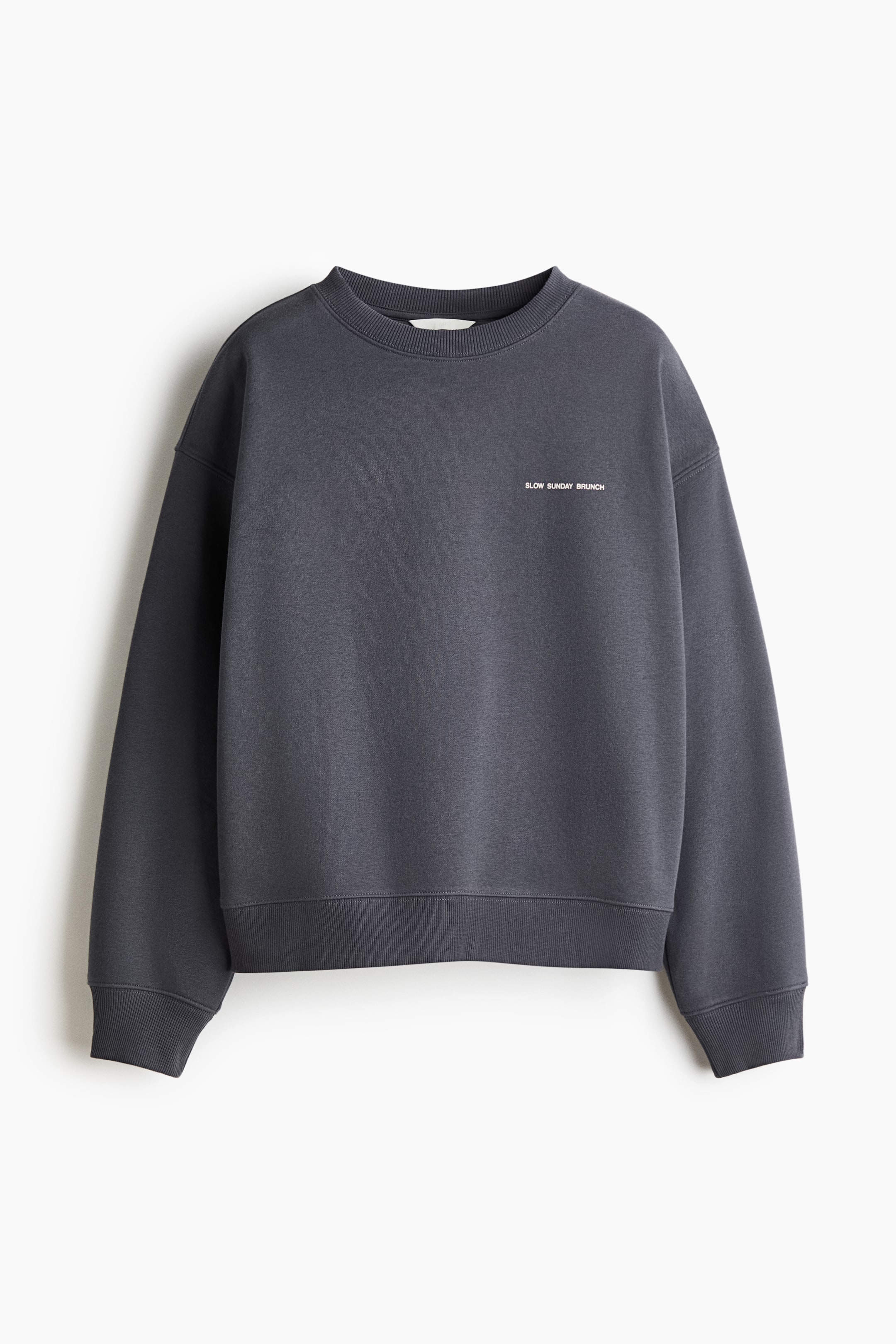 View larger image: A dark gray oversized sweatshirt is presented FRONT, featuring a round, rib-trimmed neckline, dropped shoulders, and long sleeves. The chest area is displaying the white text "SLOW SUNDAY BRUNCH," and ribbing is visible at the cuffs and hem.