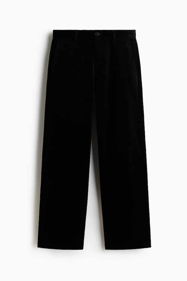 Black corduroy trousers are displayed front-facing. They feature a waistband with belt loops, a single button fastening, and angled side pockets. The trousers are designed with a wide-leg fit. - 1
