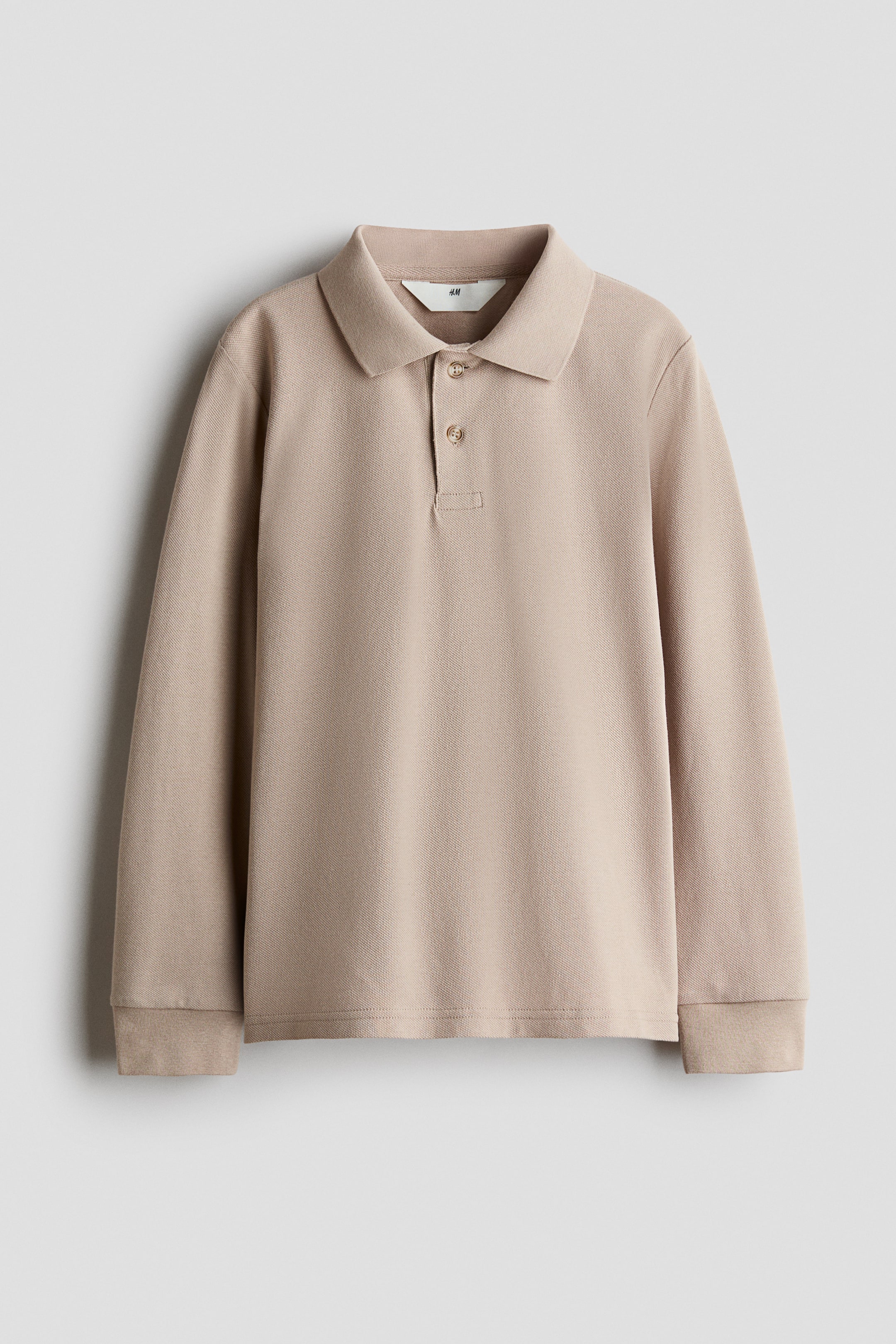 Größeres Bild anzeigen: Ein langärmliges Poloshirt in leicht beigem, strukturiertem Strick hängt frontseitig und verfügt über einen klassischen Kragen mit einer Zweiknopfleiste. Das Shirt zeigt lange Ärmel mit Rippbündchen und einen geraden Saum.