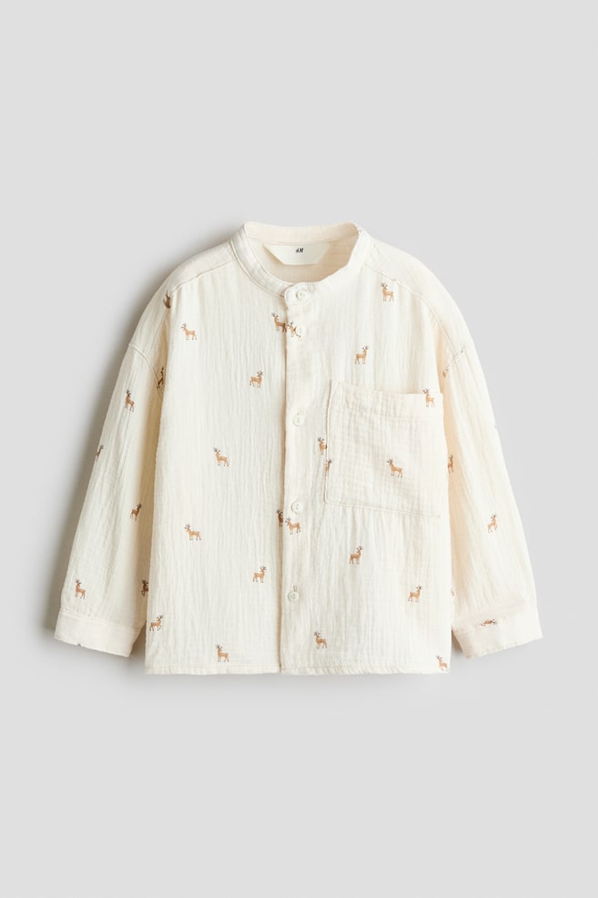 Una camicia color bianco sporco a maniche lunghe, in un tessuto di garza di cotone increspata dalla texture materica, è mostrata frontalmente e presenta una stampa all-over di piccoli cervi marroni. La camicia sfoggia un collo alla coreana, apertura frontale con bottoni, spalle scese e una singola tasca applicata sul lato sinistro del petto. - 1