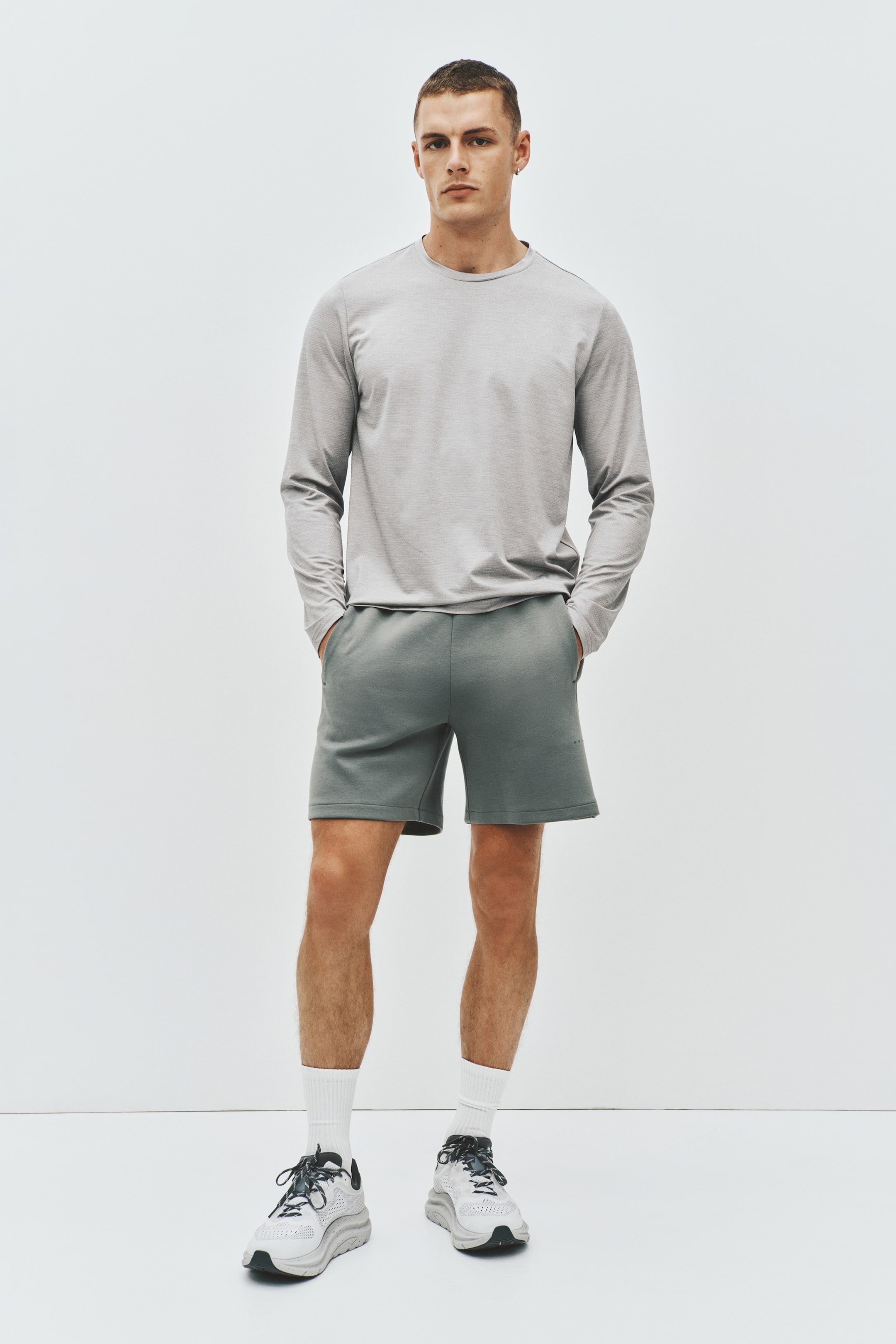 View larger image: A light grey long-sleeve crew neck t-shirt, featuring a subtle heathered texture and a regular fit, is displayed from a front-facing angle, paired with dark grey relaxed-fit shorts that extend above the knee.