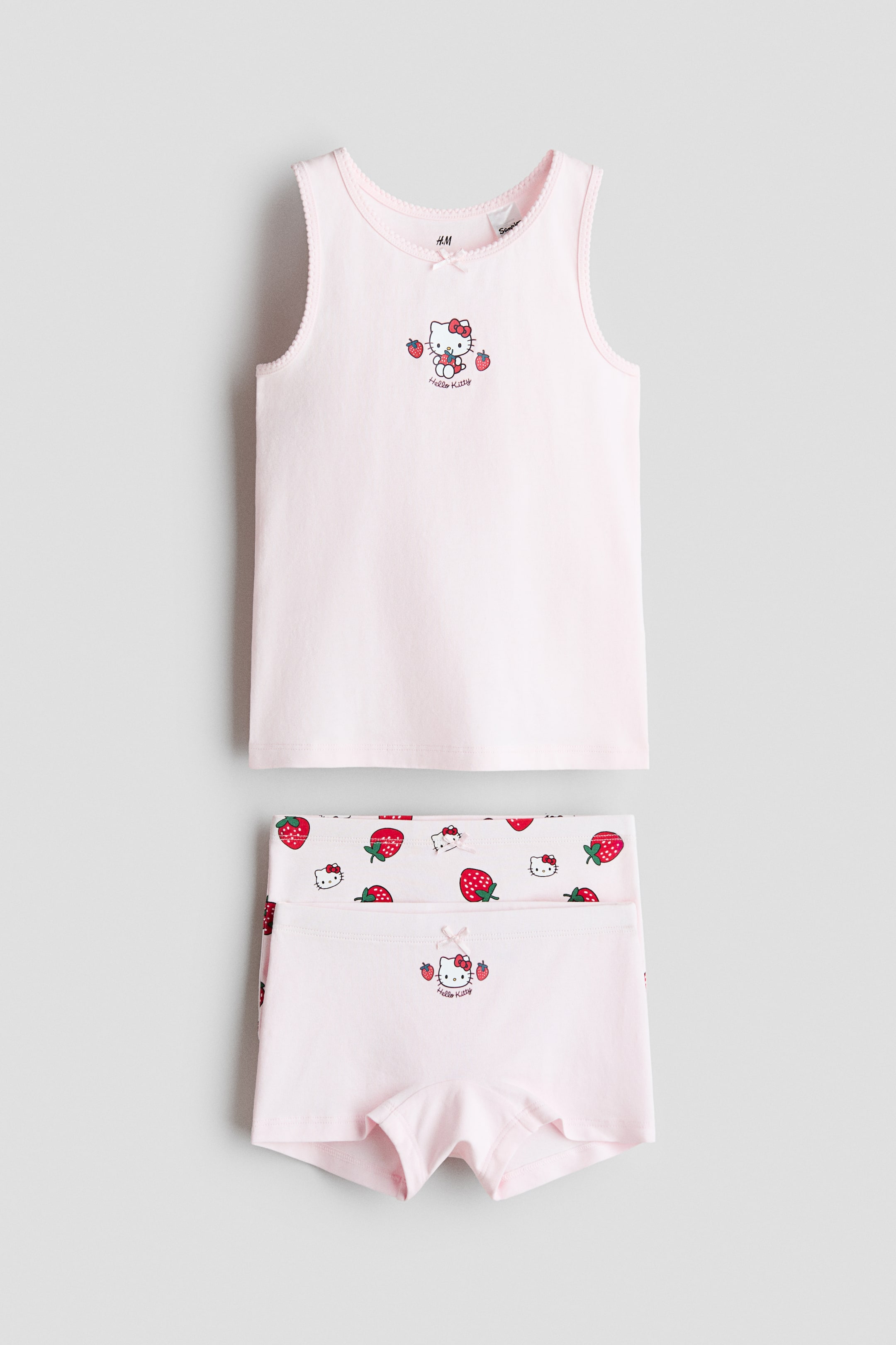 View larger image: A set comprising a light pink vest top and two pairs of matching briefs is on display, facing front. The vest top showcases a Hello Kitty and strawberry print motif at the centre front, with picot trim around the neckline and armholes. Both pairs of briefs feature elasticated waists; one brief displays an all-over Hello Kitty and strawberry pattern, while the other presents a central Hello Kitty and strawberry motif on its front.