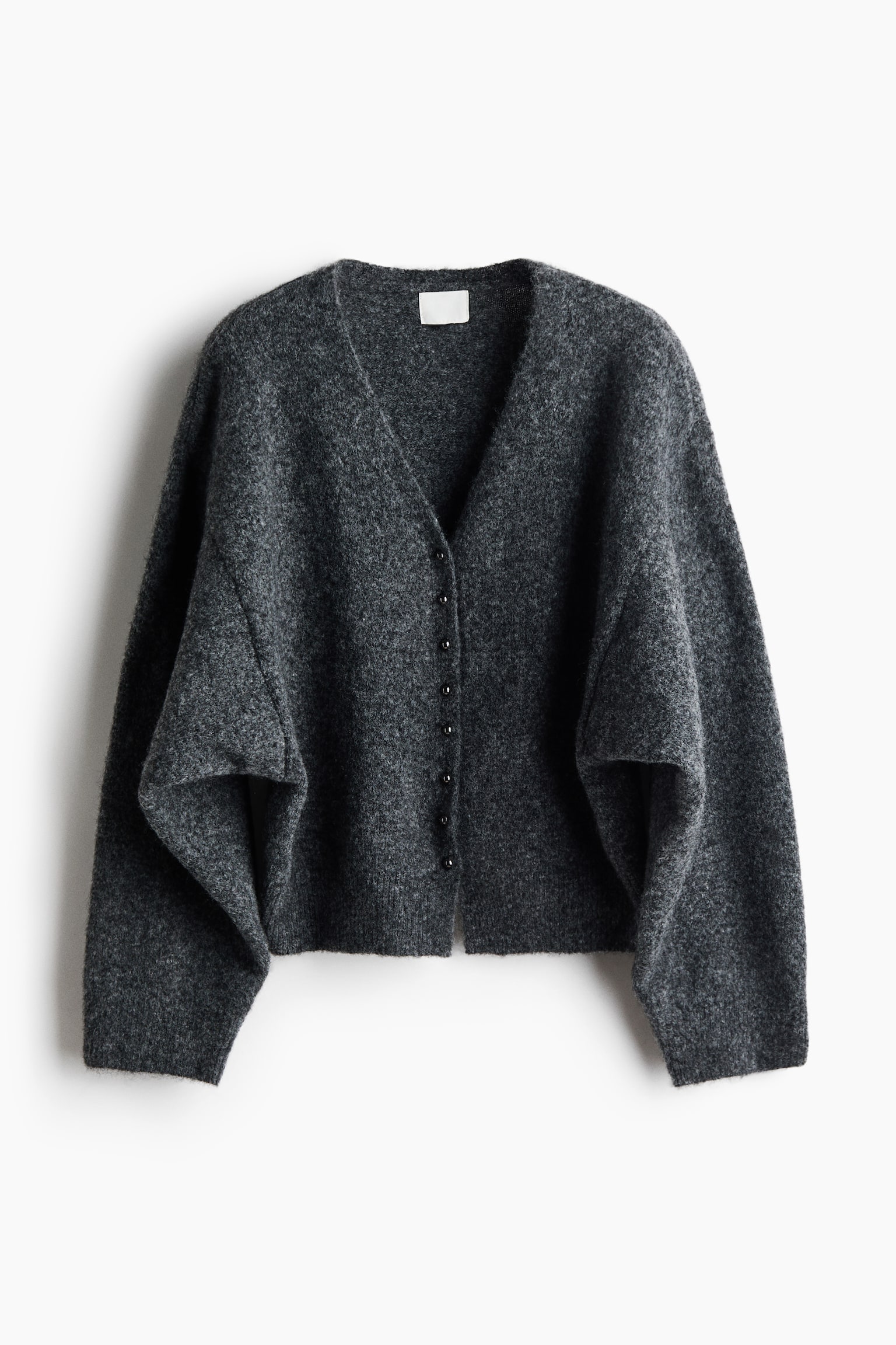 Eine dunkelgraue, flauschige Strickjacke ist frontal zu sehen und verfügt über einen tiefen V-Ausschnitt sowie einen vorderen Verschluss mit kleinen, dunklen Knöpfen. Die Strickjacke zeigt eine oversized, entspannte Silhouette mit weiten, lässig fallenden Ãrmeln und gerippten Bündchen an den Ãrmelabschlüssen und am Saum.