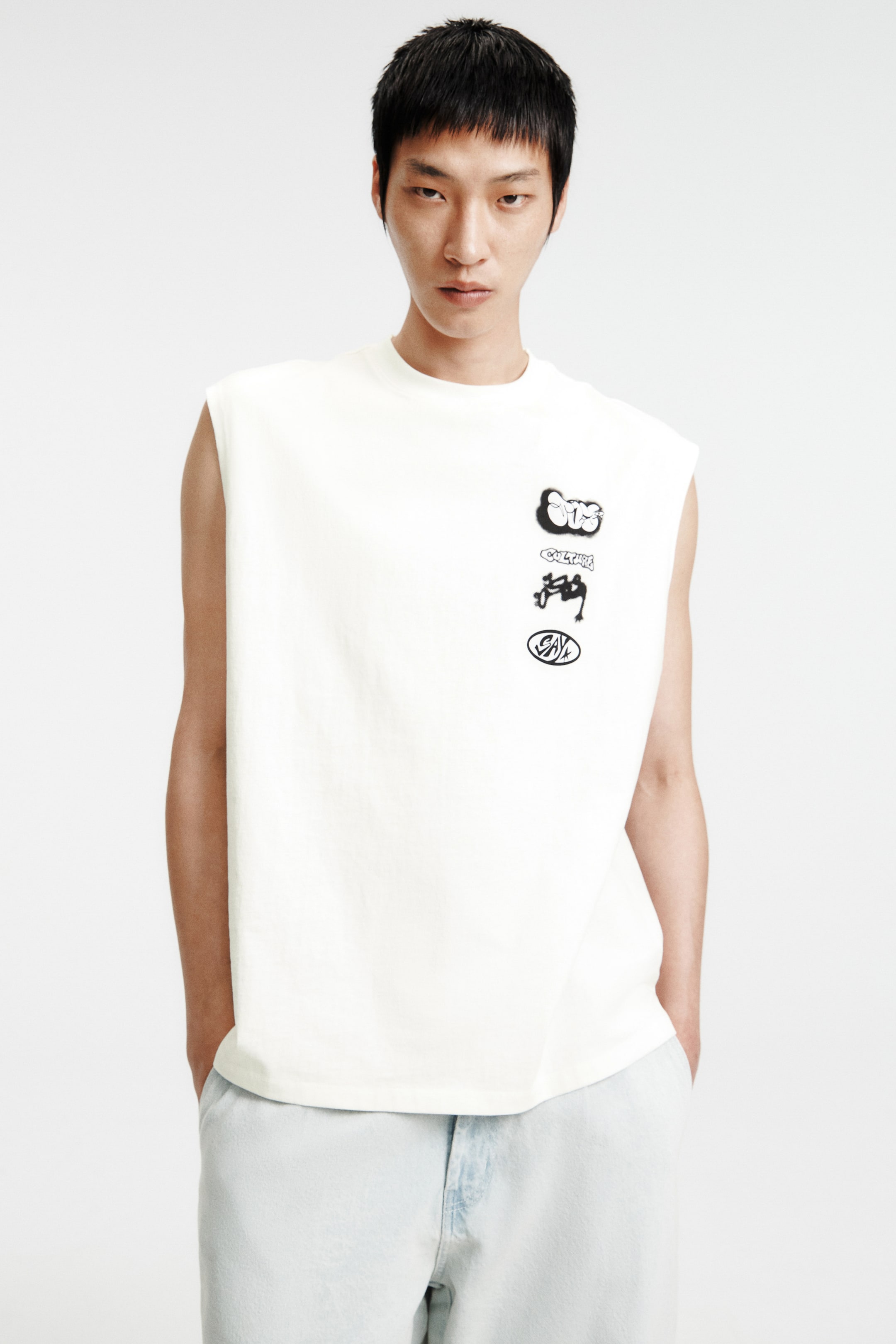View larger image: A sleeveless top in off-white is showcased from the front, highlighting a crew neck and a relaxed silhouette. On the front, there is a vertical arrangement of four unique black graphic designs, with the straight hemline reaching hip length.