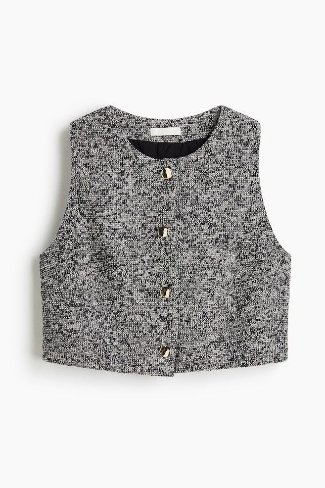 A black and white tweed vest is displayed front-facing, featuring a round neckline, a cropped hem, and five gold-toned buttons down the front. - 1