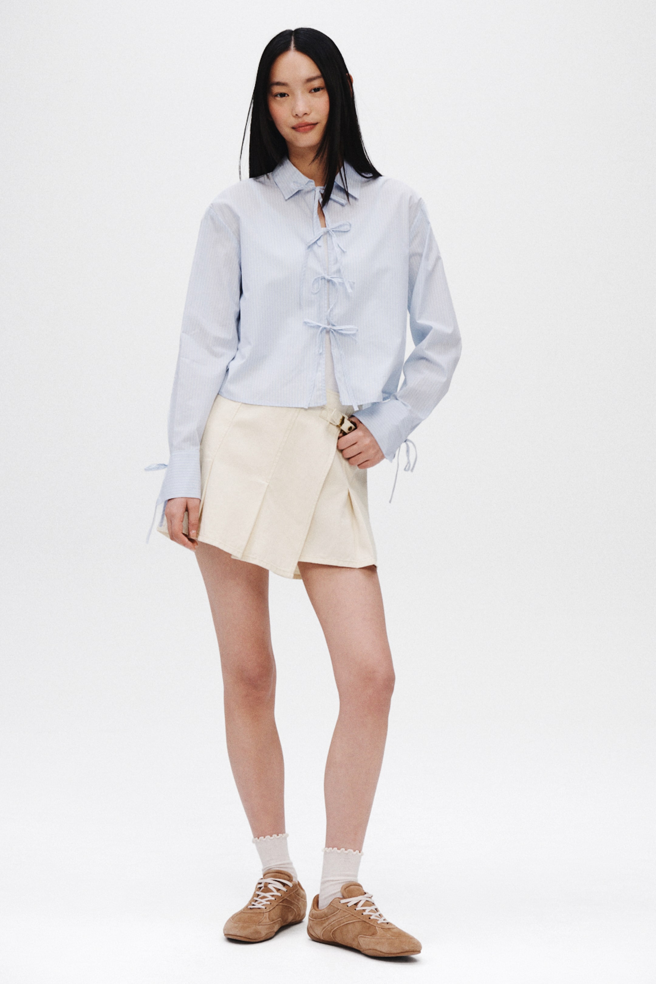 查看大圖: 淺藍色條紋襯衫，設有領子、沿前中心的三個可綁成蝴蝶結的前綁帶、長袖袖口的綁帶細節，以及短款剪裁。