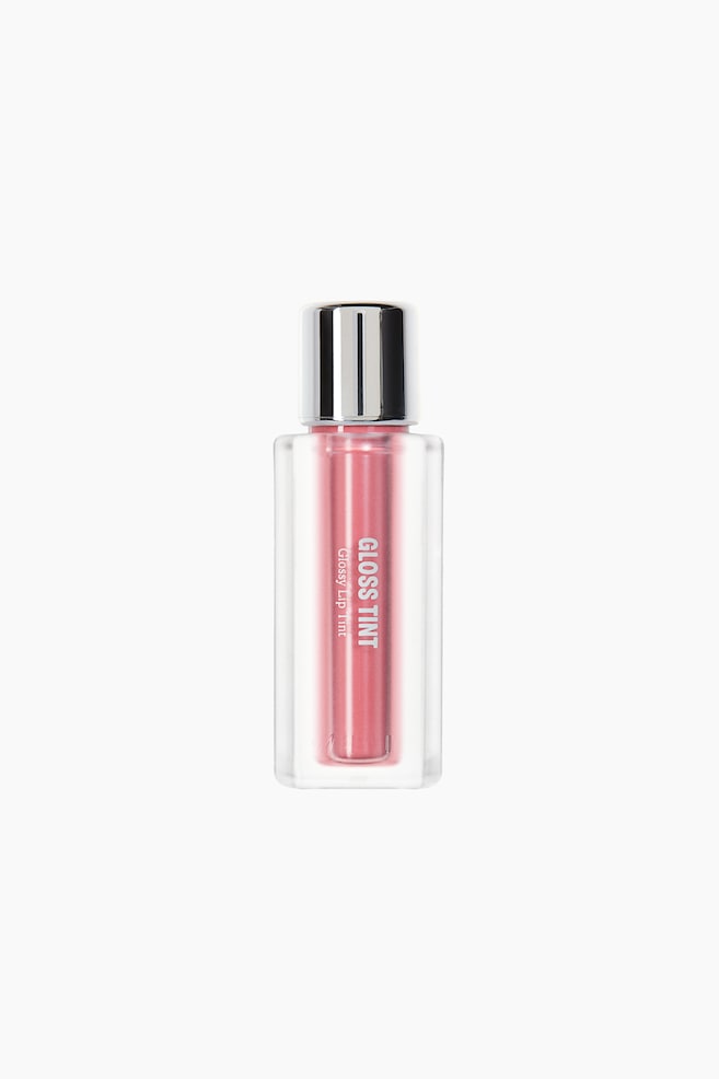A bottle of pink lip tint stands upright, facing forward, featuring a rectangular frosted clear container that reveals a central pink reservoir inside. The container is topped with a cylindrical metallic silver cap and displays vertical white text reading âGLOSS TINTâ and âGlossy Lip Tintâ on the front. - 1