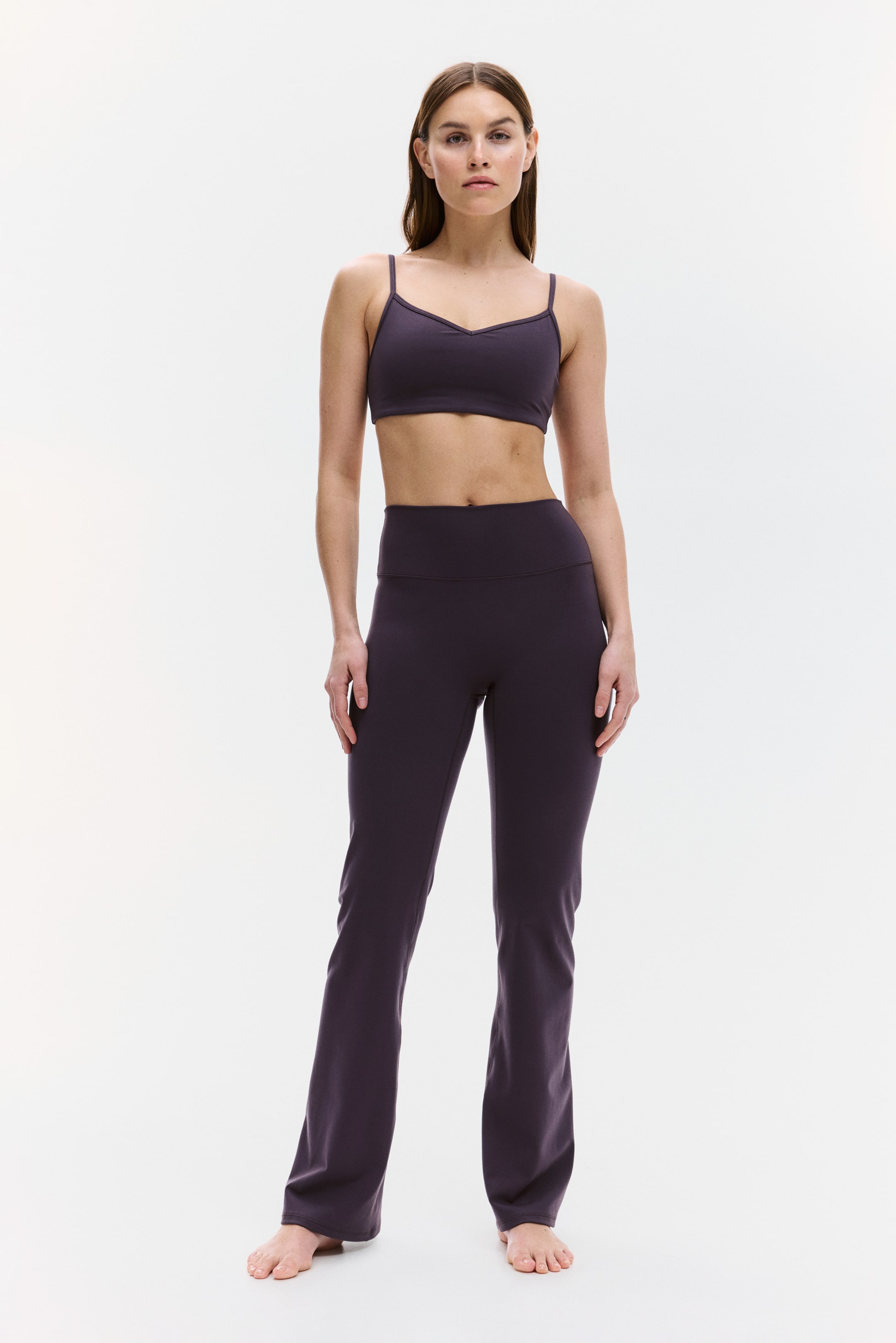 View larger image: A deep purple activewear set is displayed in a full-front view, comprising a sports bra and yoga pants. The sports bra features a V-neckline and thin spaghetti straps, while the high-waisted yoga pants come with a broad waistband and a flared leg design.