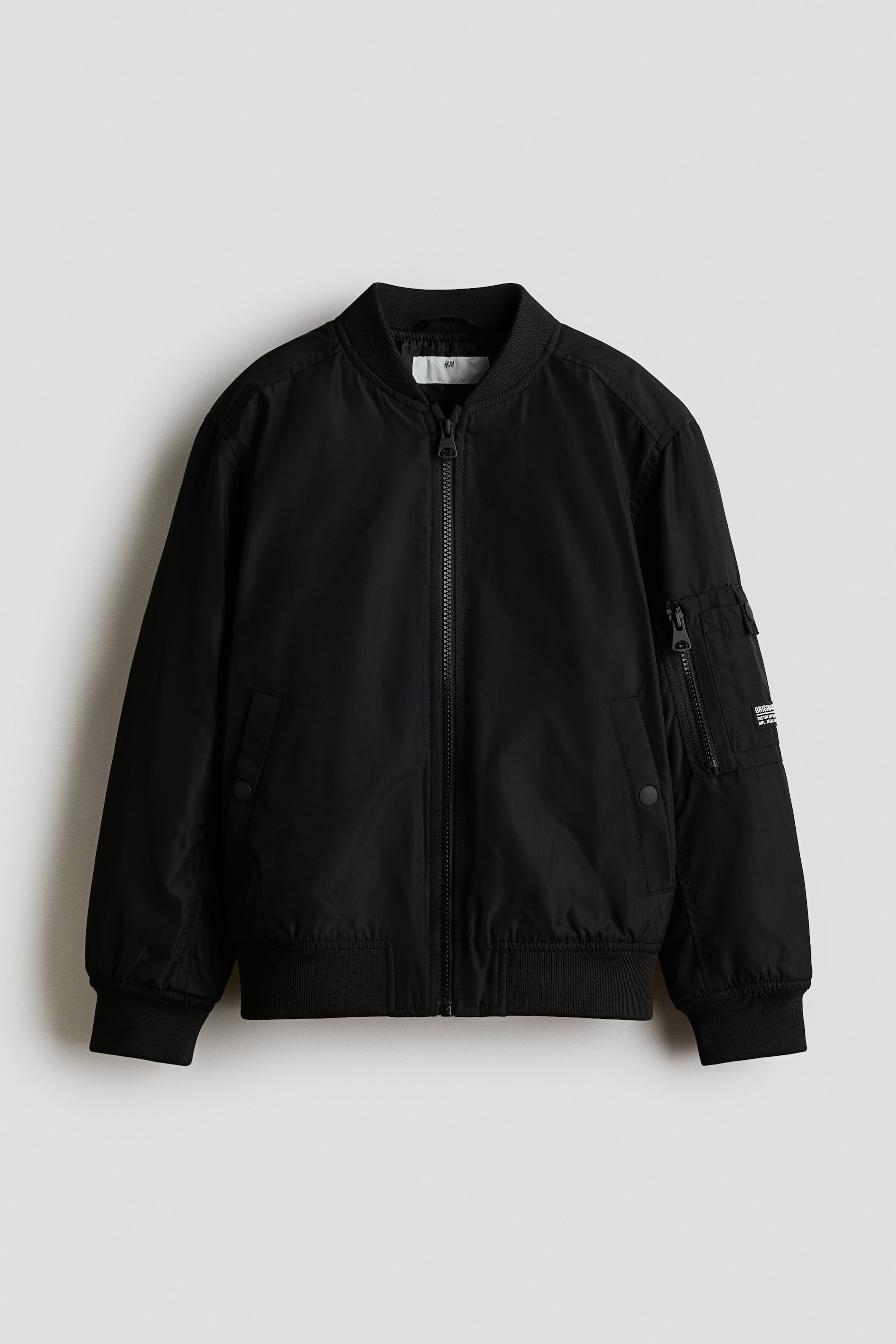 View larger image: A black bomber jacket is presenting its FRONT view, featuring a slight sheen, a ribbed stand collar, and a central zip closure. It is displaying two welt side pockets with press-studs, a double pocket with zipped and press-stud fastened compartments on one long sleeve, dropped shoulders, and wide ribbed jersey trims at the cuffs and hem.