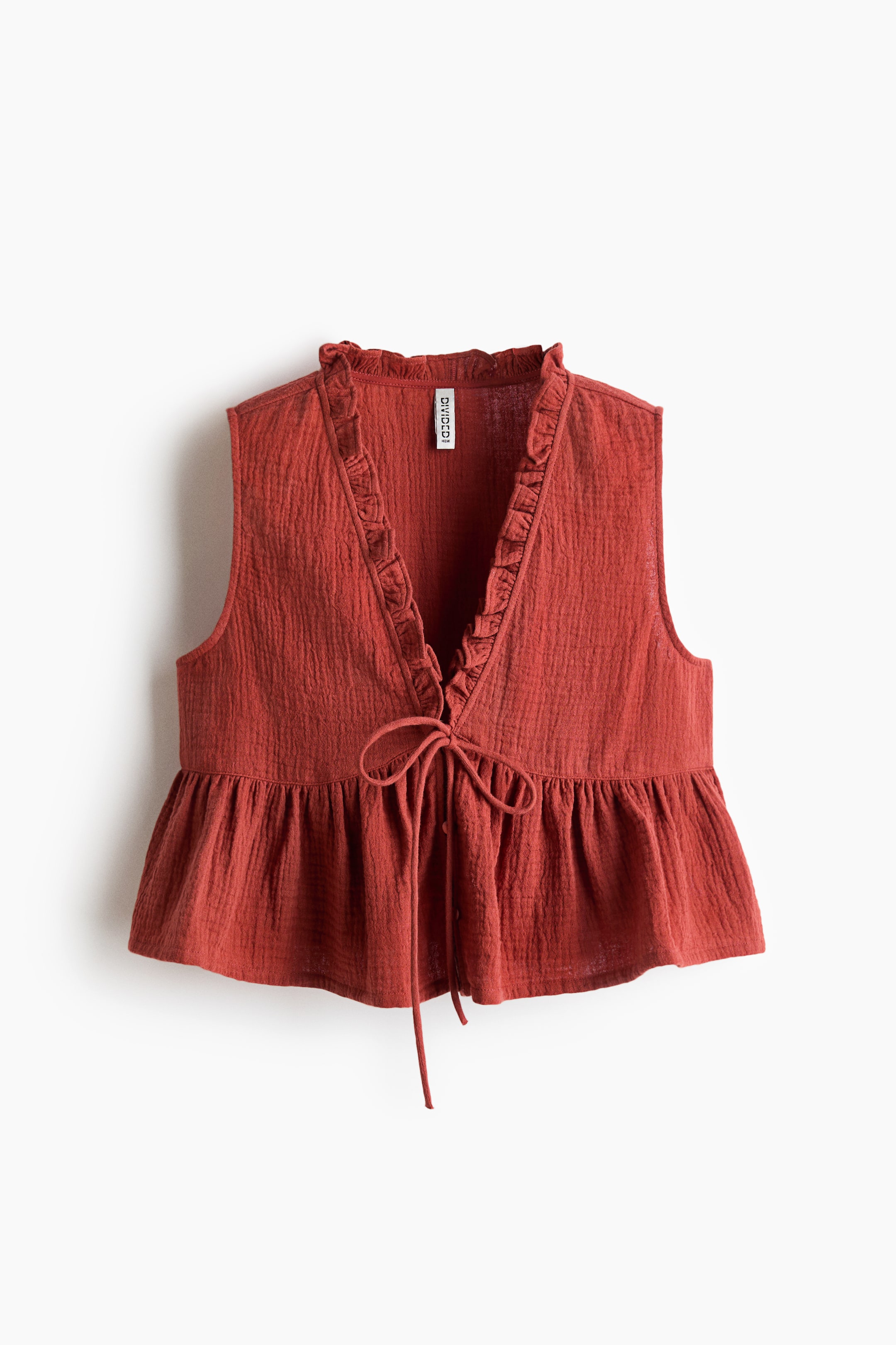 View larger image: A rust-coloured sleeveless top is shown from the front. It features a ruffled V-neckline, a tie-front closure and a gathered peplum hem, all crafted from crinkled fabric.