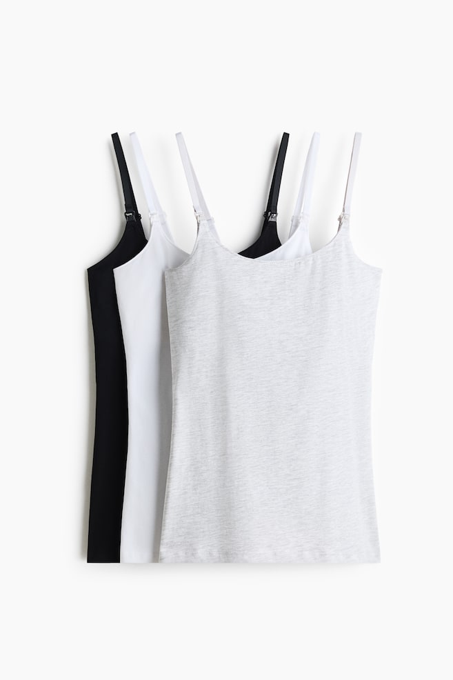 Three nursing camisoles in black, white and light grey melange are overlapping in a layered front view. Each camisole features narrow, adjustable shoulder straps with small nursing clasps at the front base for convenient access. - 1