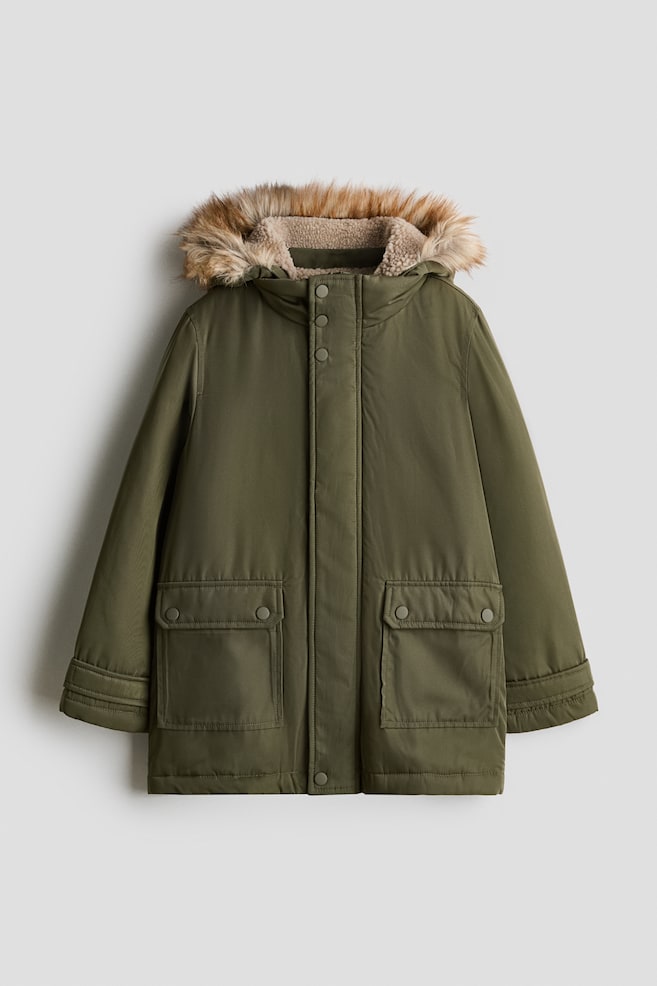 Eine olivgrÃ¼ne Parka-Jacke ist von vorne zu sehen und zeigt eine Kapuze mit hellbeigem Sherpa-Fleece-Futter und braunem Kunstfellbesatz. Die Jacke verfÃ¼gt Ã¼ber einen verdeckten FrontreiÃverschluss mit DruckknÃ¶pfen sowie zwei groÃe aufgesetzte Taschen im unteren Bereich mit Patten und Druckknopfverschluss. - 1