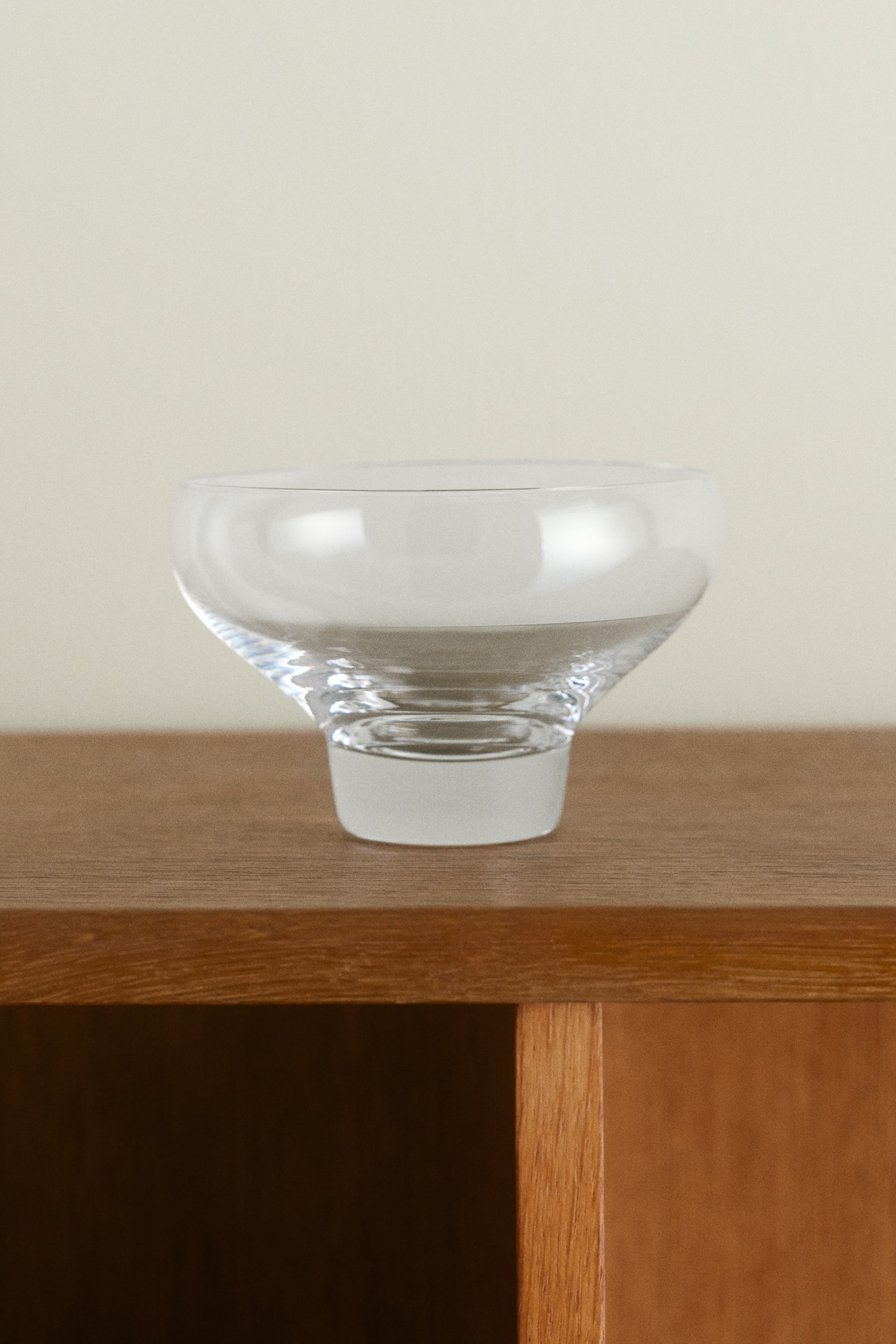 View larger image: A mouth-blown clear glass bowl stands upright, showcasing a wide, rounded basin that tapers down to a thick, solid cylindrical base.
