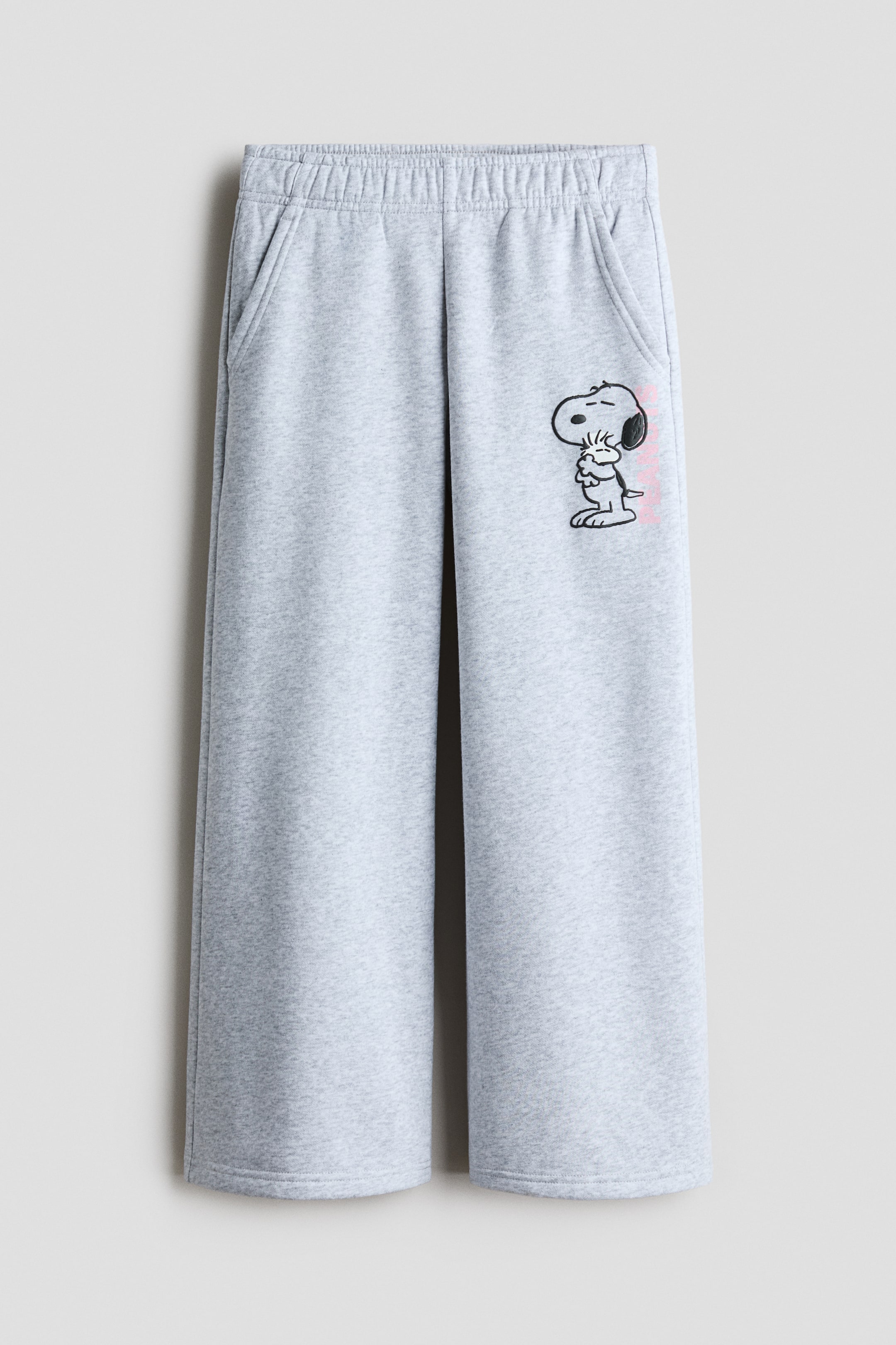 View larger image: The grey sweatpants are shown in a front view, showcasing an elasticised waistband and two angled side pockets. Their wide legs extend to plain hems, and a Snoopy graphic with pink text appears on the upper right leg.