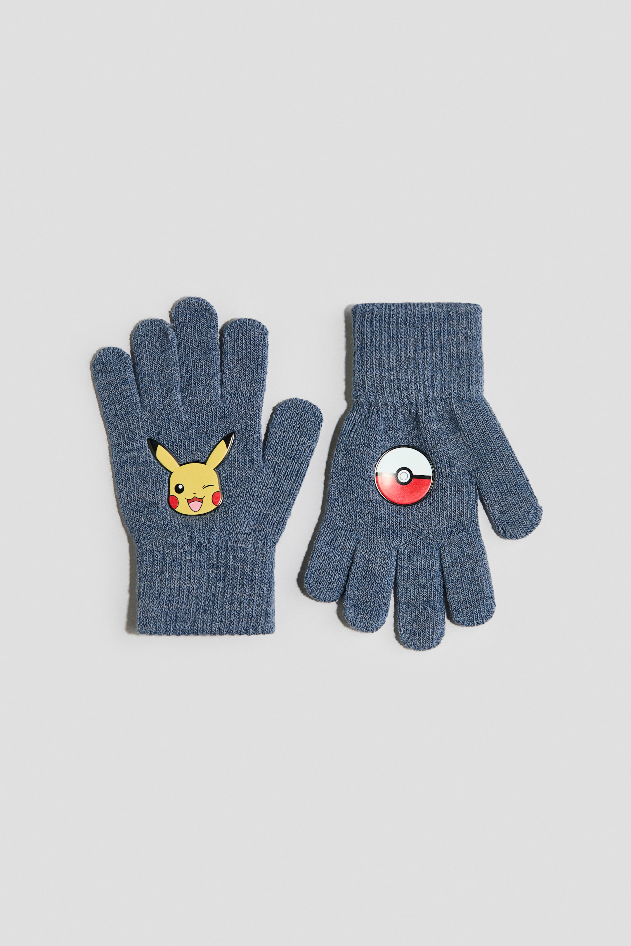 Näytä suurempi kuva: Pari sinisiä neulottuja käsineitä on aseteltu litteästi etupuoli kameraan päin. Vasen käsine on koristeltu keltaisella, silmää iskivällä Pikachu-naamalla, kun taas oikeassa käsineessä on punainen, valkoinen ja musta Poké-pallon tunnus.