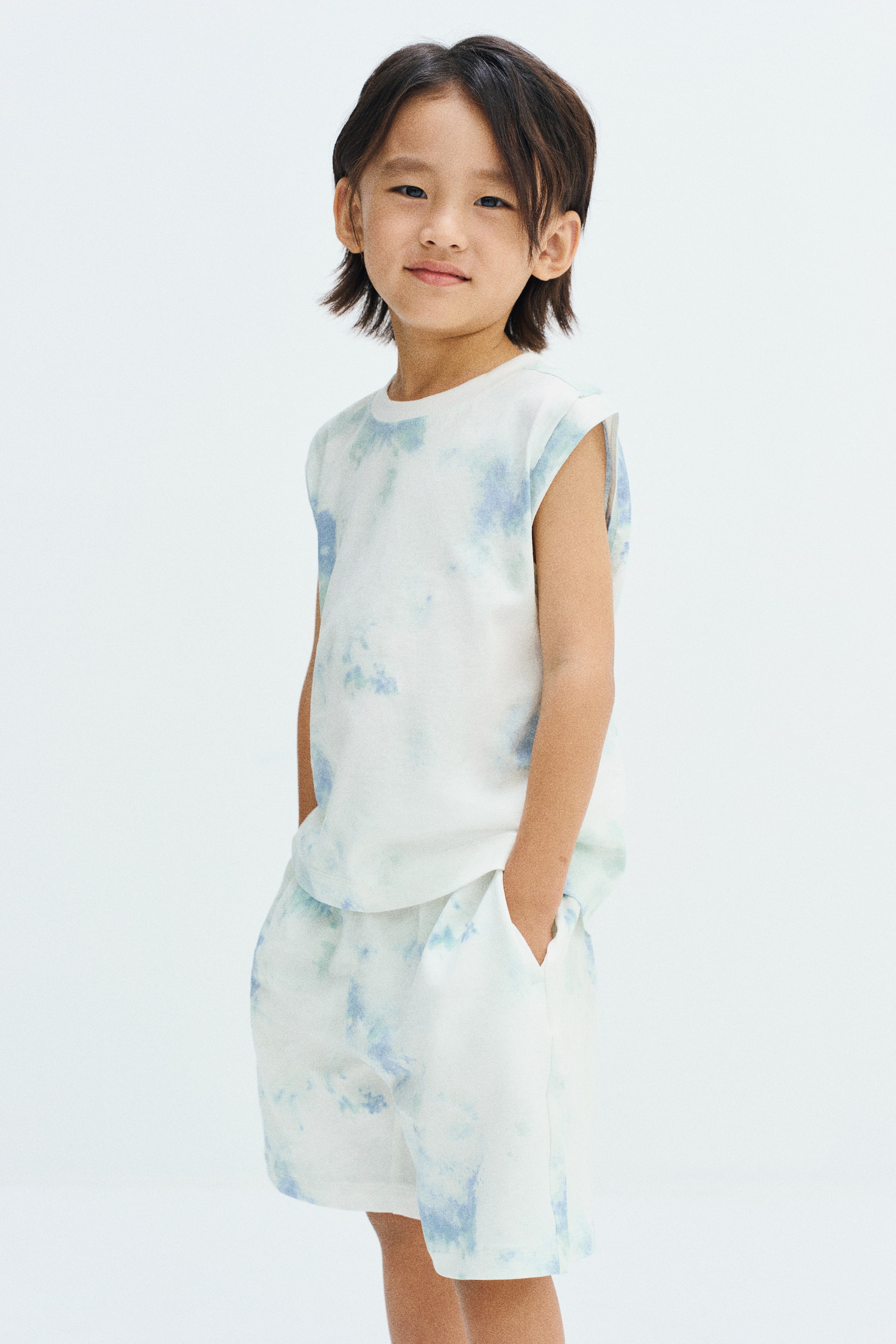 View larger image: A sleeveless tank top featuring a blue and white tie-dye pattern and a round, rib-trimmed neckline is worn by the model. The top is paired with matching tie-dye shorts.