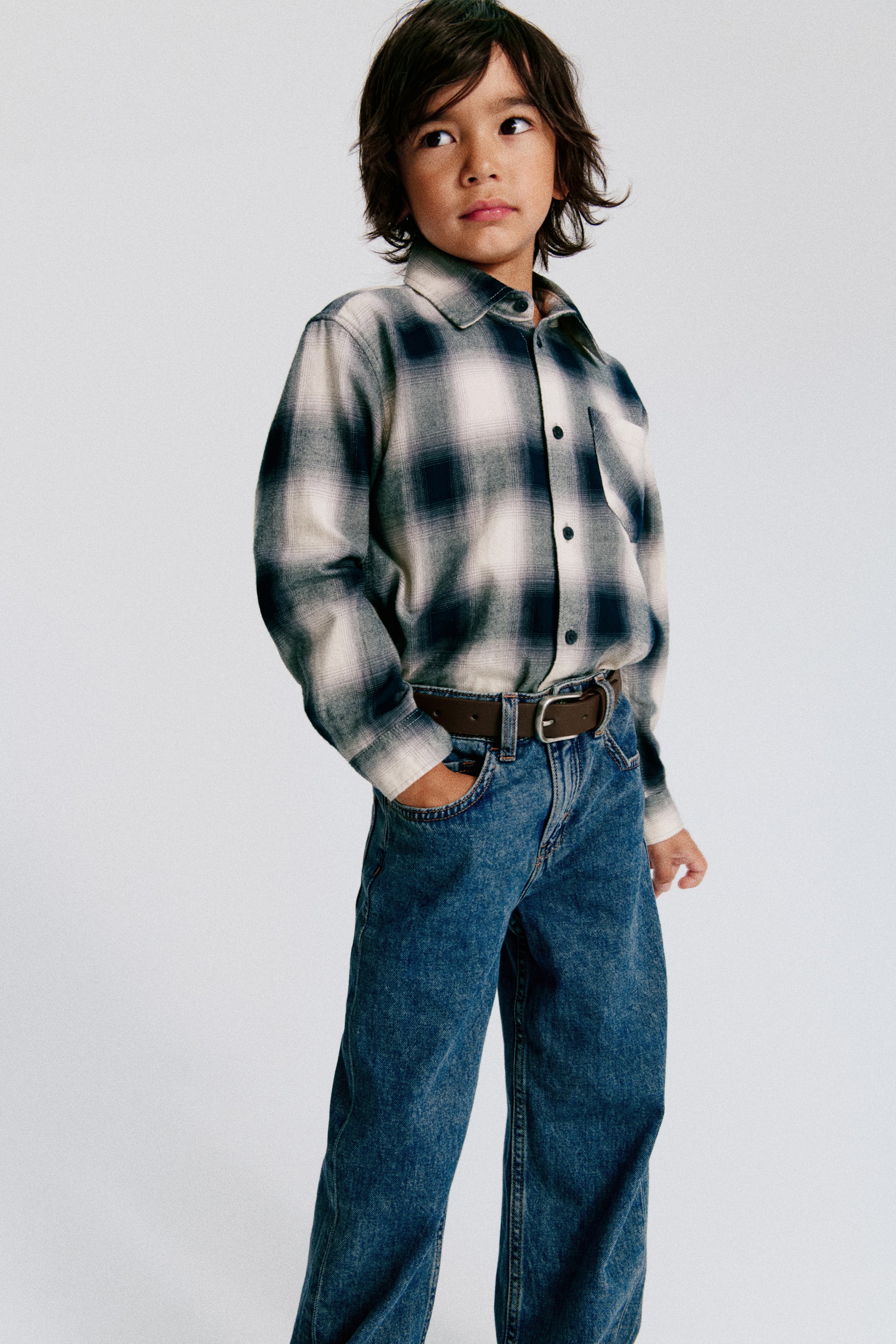 View larger image: Five-pocket jeans in blue washed soft cotton denim are presented in a loose fit through the hip and thigh with a dropped crotch, seen from the front. A brown belt is threaded through the visible belt loops, and a zip fly is partially visible.
