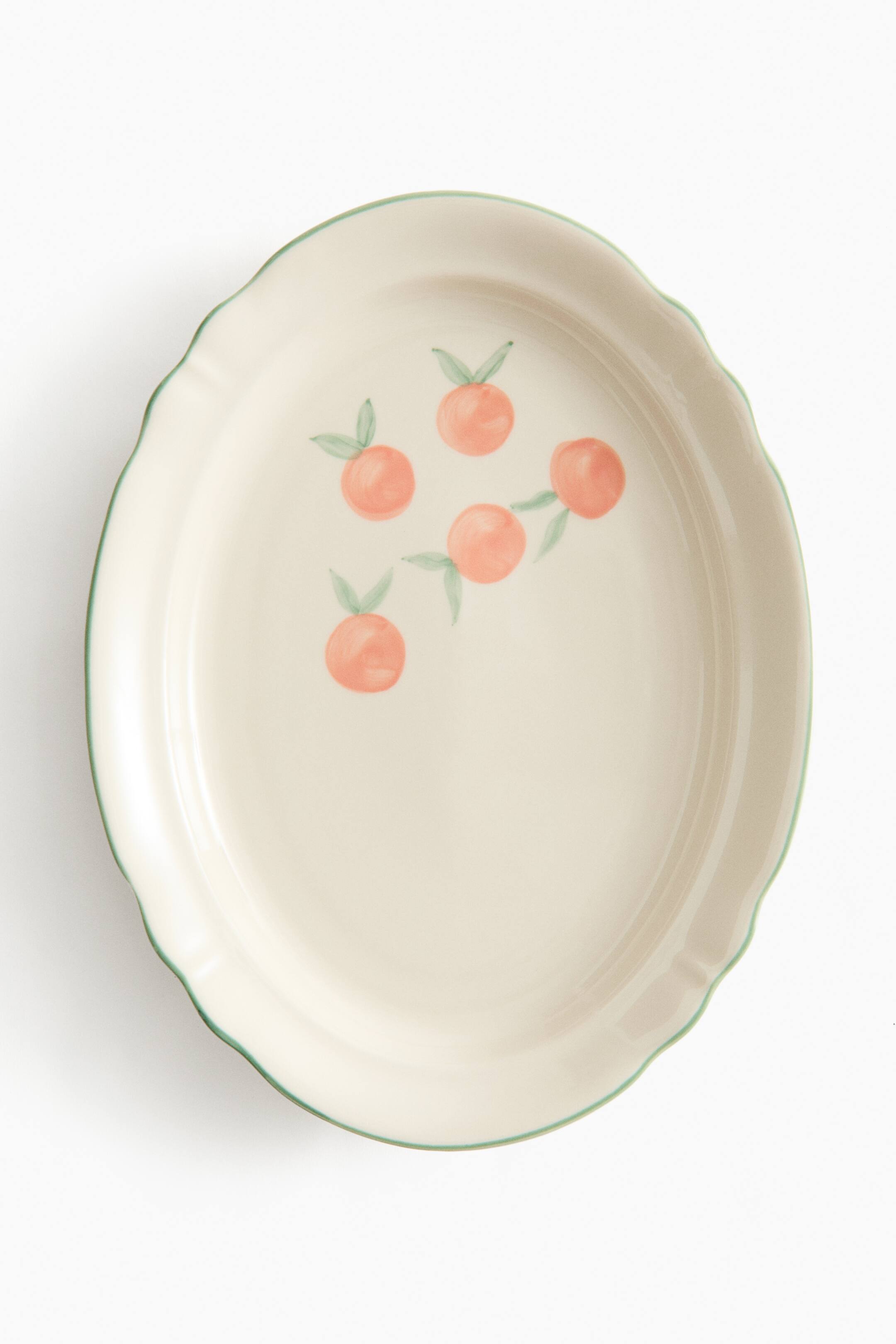 Agrandir l'image: Un plat de service ovale présente une surface couleur crème et un rebord festonné. Le rebord est souligné d'une bordure verte peinte à la main, et cinq motifs de fruits orange aux feuilles vertes parsèment la surface du plat.