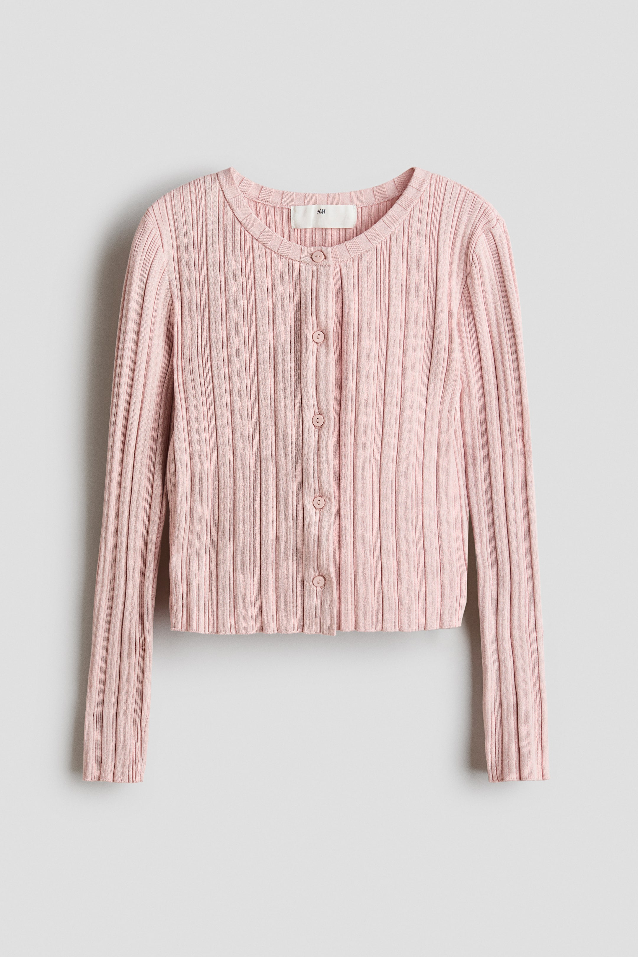 Vis større bilde: En rosa cardigan viser sin front, med en uregelmessig ribbestrikk, rund hals, knappelukking foran og lange ermer. Rå kanter avslutter mansjettene og falden.