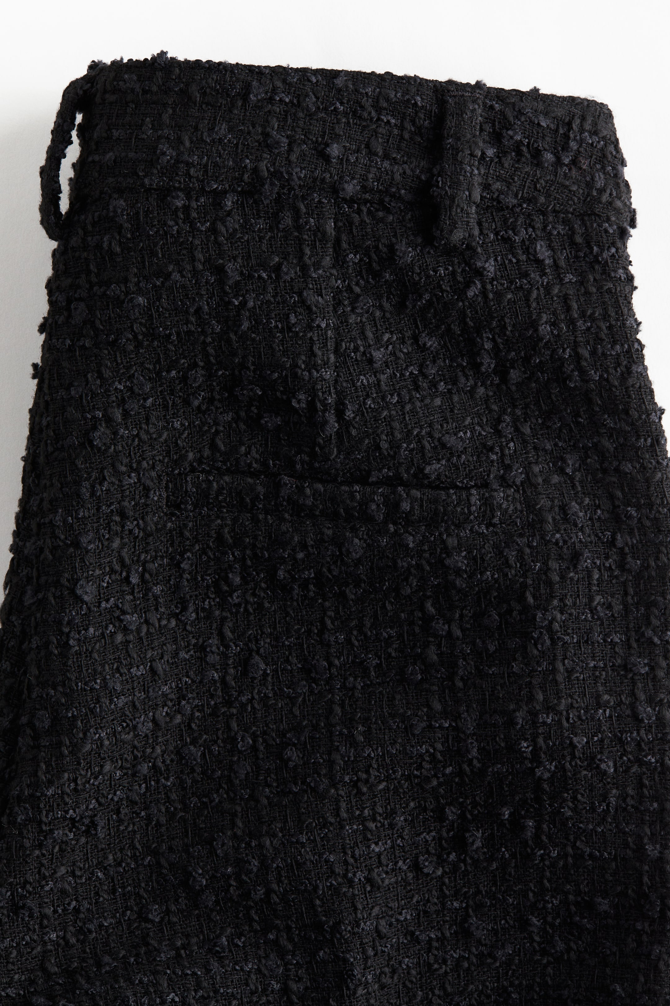 View larger image: A black garment, featuring a heavily textured bouclé fabric, is displaying its front with a waistband, multiple belt loops, and a flat front panel.