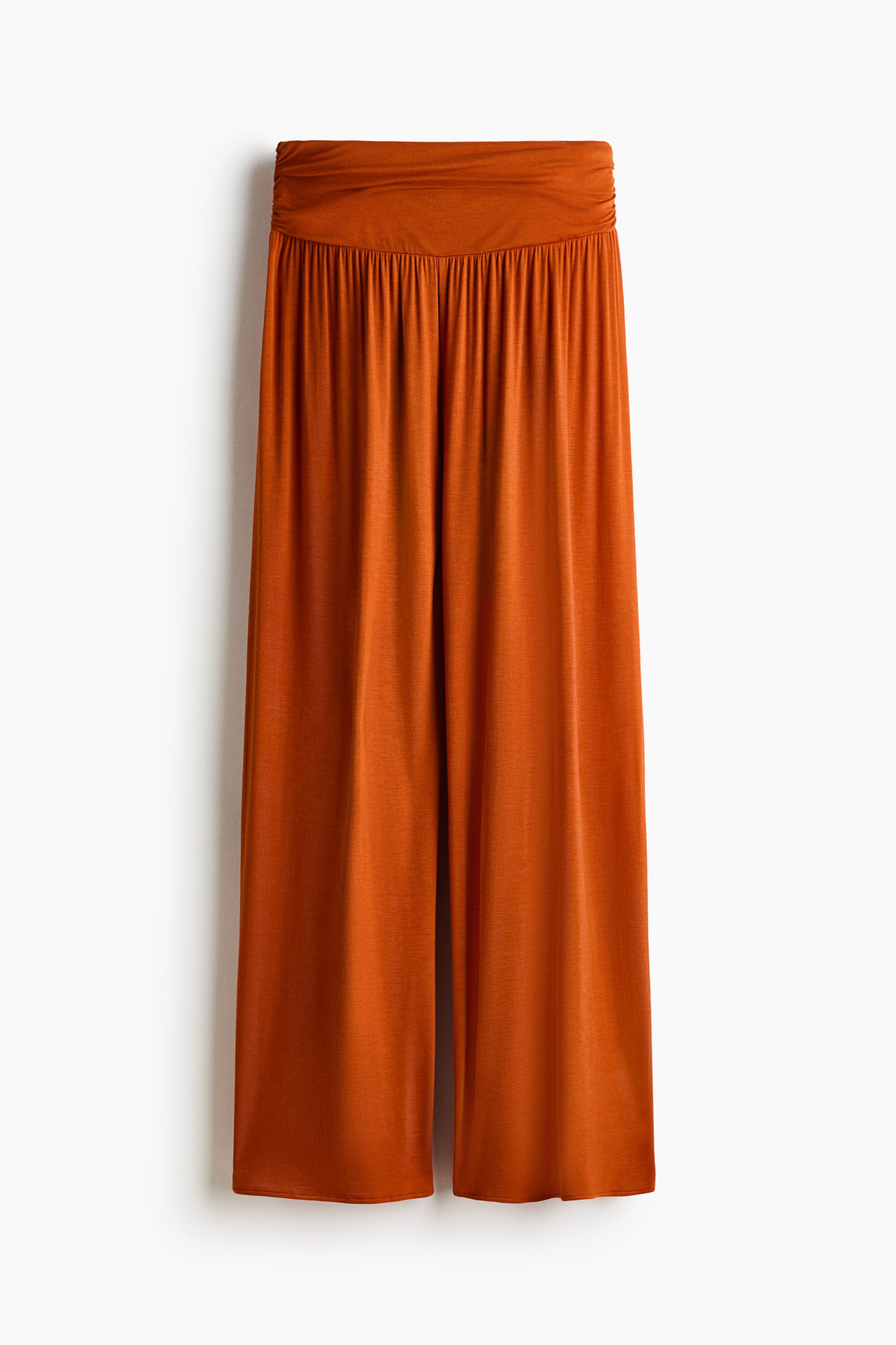 View larger image: Front view of a pair of burnt-orange pants, featuring a wide, smooth waistband with gathering directly beneath it and wide, flowing legs.