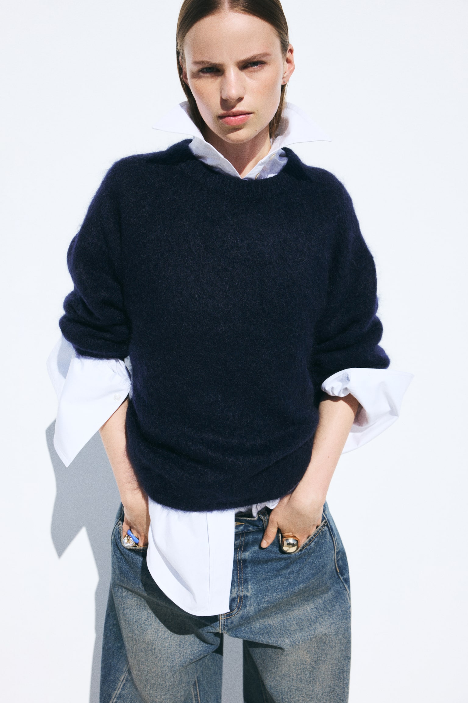 Un maglione in maglia morbida di colore blu scuro Ã¨ indossato dalla modella, sovrapposto a una camicia bianca con colletto e abbinato a jeans blu. Il maglione oversize presenta spalle scese, girocollo a costine e polsini a costine. - 1