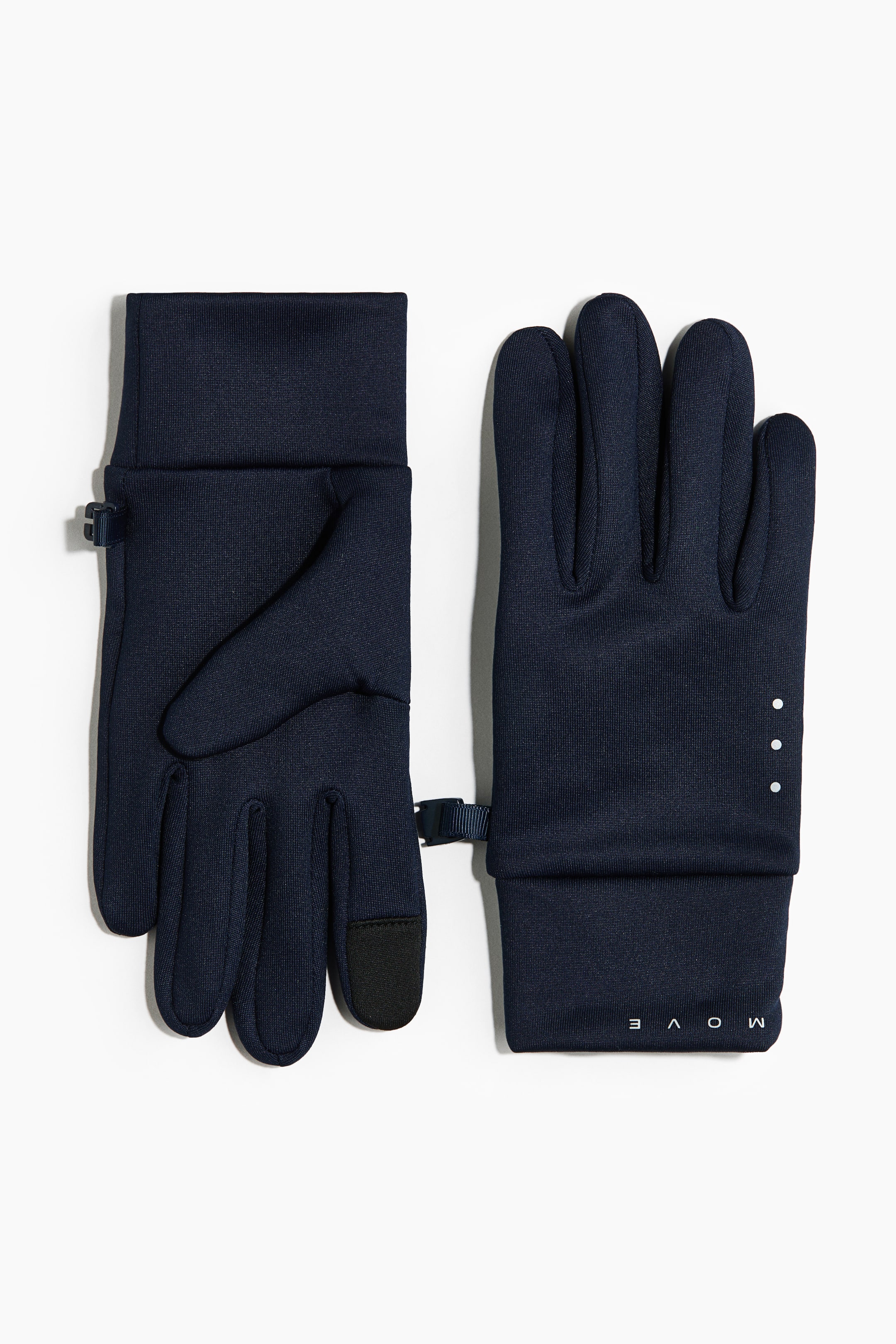 Voir une image plus grande: Une paire de gants de performance bleu marine est présentée de face et de dos, avec des poignets allongés et de petites sangles ajustables avec boucles au niveau du poignet. Le gant gauche montre sa paume avec des bouts de doigts noirs compatibles avec les écrans tactiles sur le pouce et l’index, tandis que le gant droit présente son dos, avec trois petits points verticaux blancs et le mot « MOVE » imprimé près du poignet.