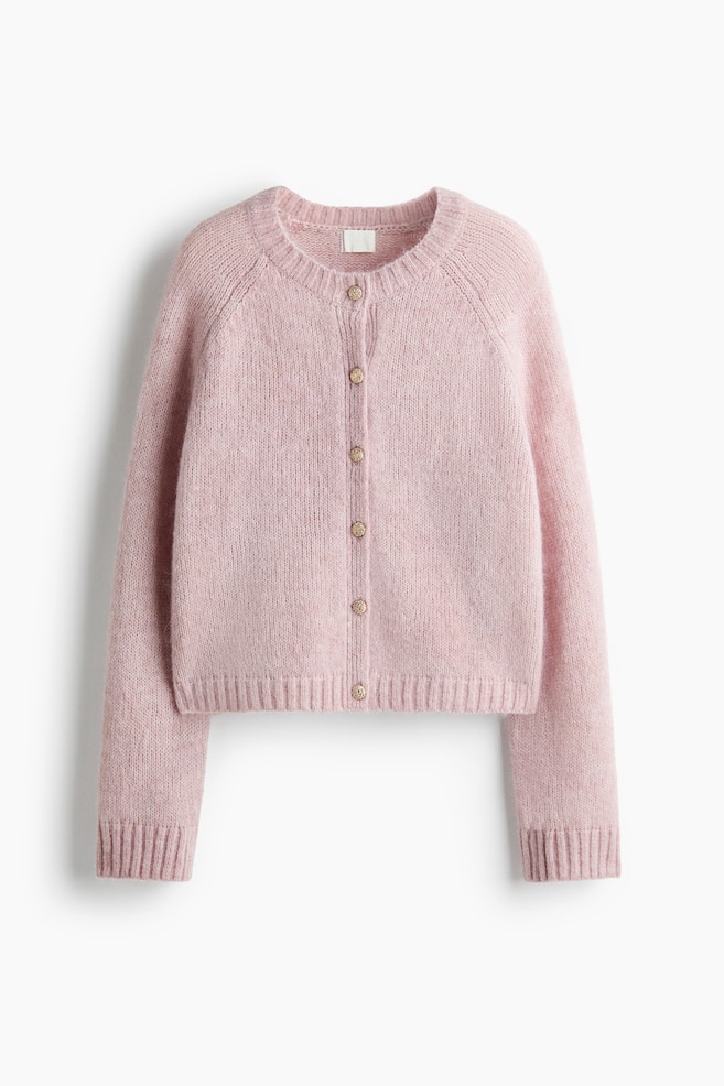A light pink knit cardigan is shown facing front, featuring a crew neckline, raglan sleeves, and a front button closure with textured gold-tone buttons. The cardigan showcases a soft, fuzzy knit texture with ribbed details on the collar, cuffs, and hem. - 1