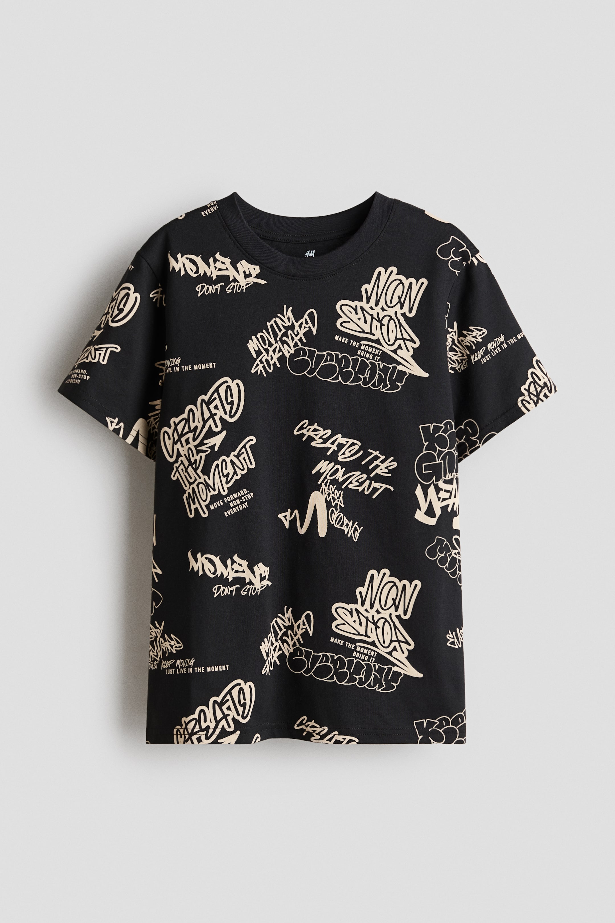 Grotere afbeelding bekijken: Een zwart klassiek t-shirt presenteert de voorkant, met een all-overprint van beige graffiti-achtige tekst over de geprinte cotton-jerseystof en zichtbaar ribboord langs de halslijn.