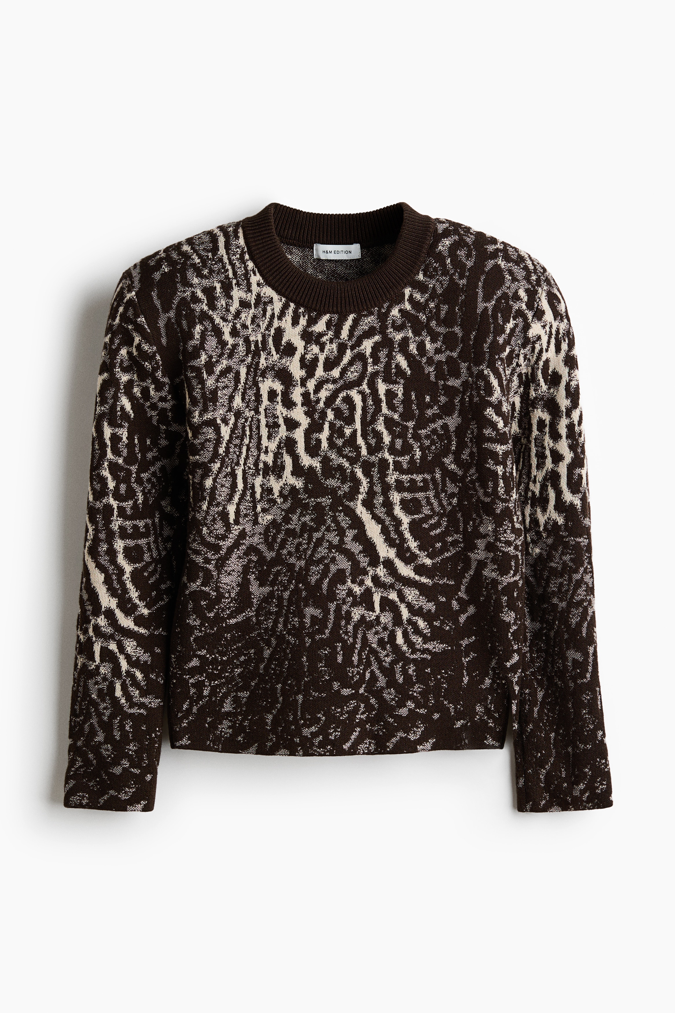 A jacquard-knit jumper with an abstract dark brown and cream pattern, a round rib-trimmed neckline and structured shoulder pads is being worn by the model.