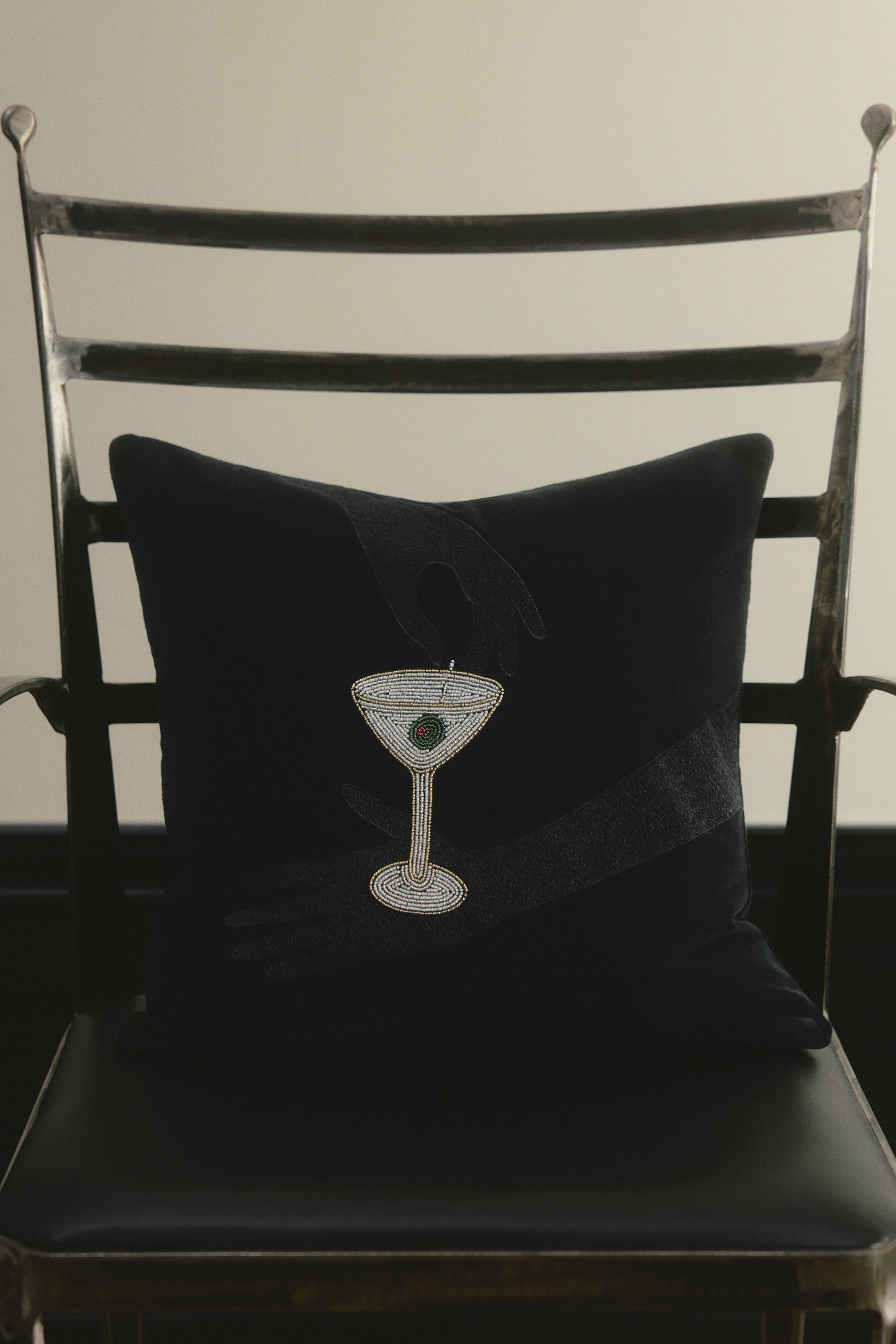 View larger image: A square black cotton velvet cushion cover is shown from the front, featuring a design of two hands holding a martini glass. The glass is detailed with shimmering white and silver bead embroidery and a green olive.