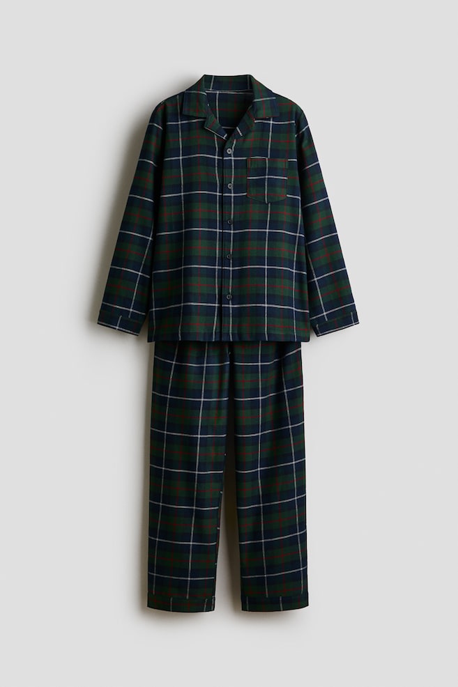 Ett tvÃ¥delat pyjamasset med rutmÃ¶nster i mÃ¶rkgrÃ¶nt, marinblÃ¥tt och rÃ¶tt hÃ¤nger vÃ¤nd framÃ¥t. Den lÃ¥ngÃ¤rmade skjortan med knÃ¤ppning fram har slag med skÃ¥ror och en enkel brÃ¶stficka, medan matchande byxor med raka ben fullÃ¤ndar setet. - 1