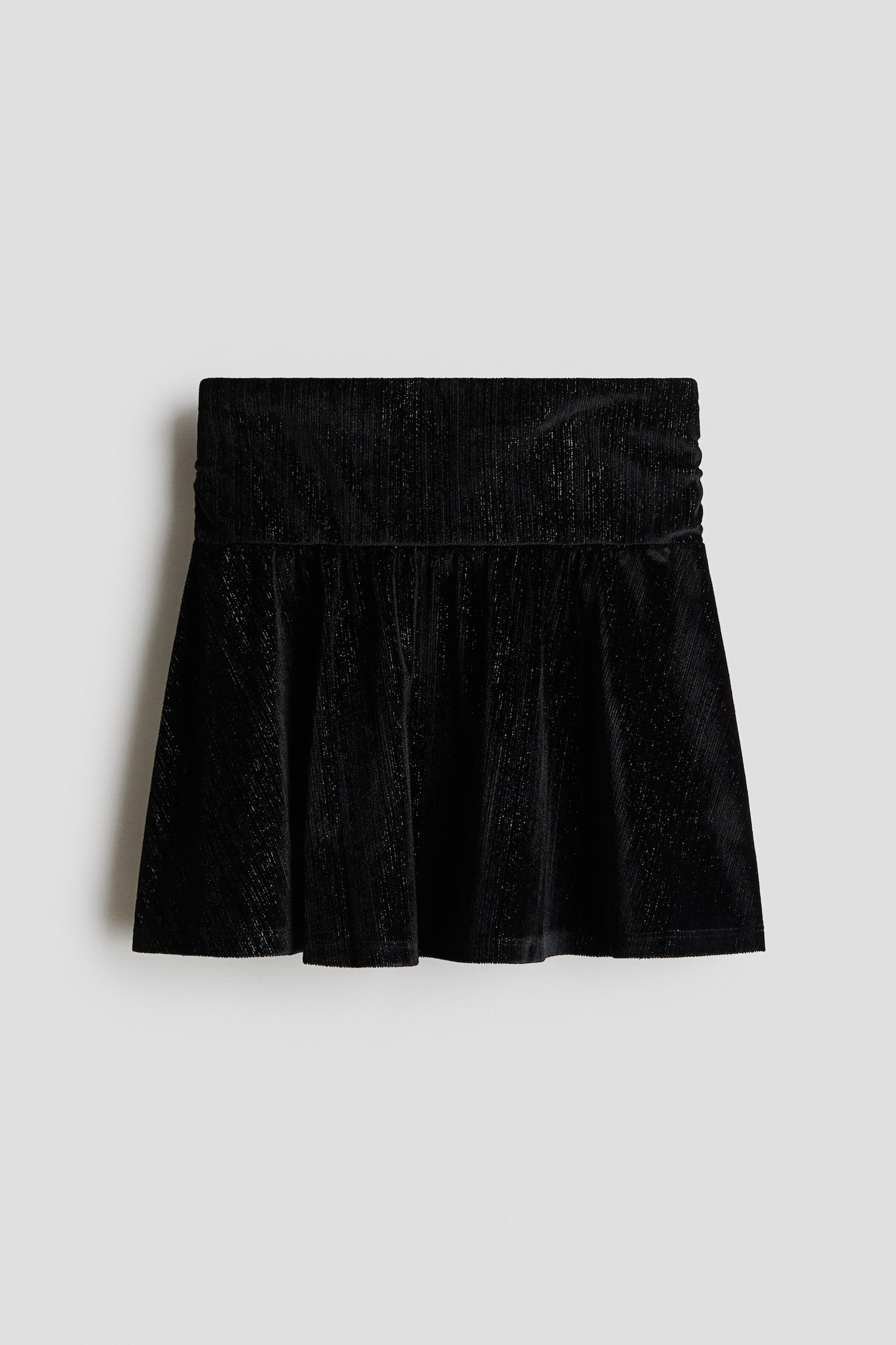A black mini skirt is shown from the front, featuring a wide, flat waistband with ruched sides and a flared, pleated lower section. The textured fabric displays a subtle shimmer with fine metallic threads running vertically throughout.