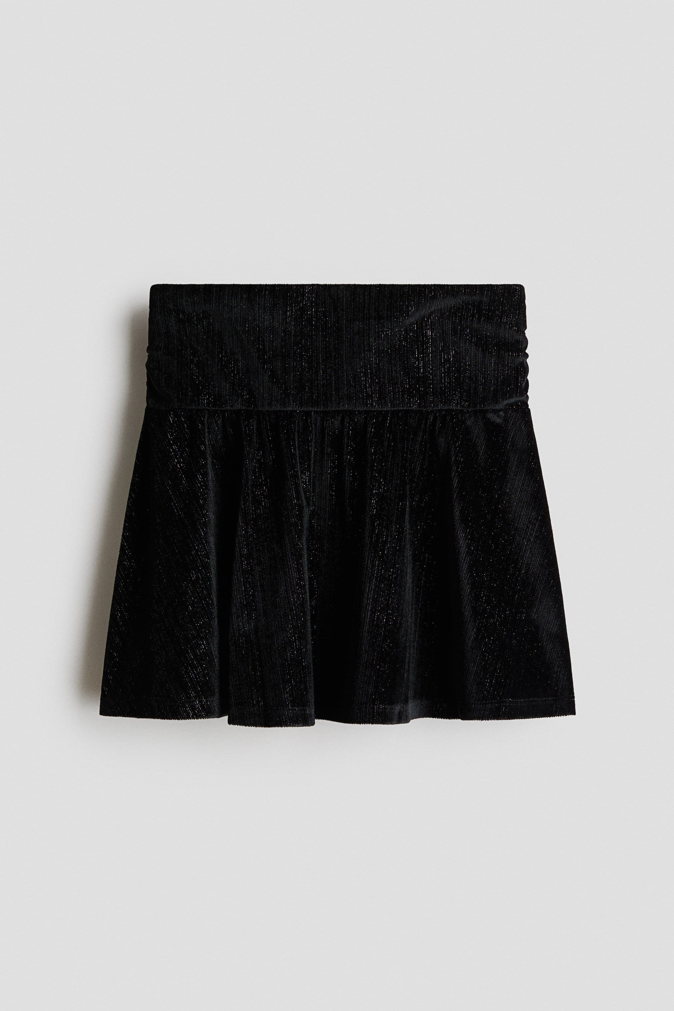 View larger image: A black mini skirt is shown from the front, featuring a wide, flat waistband with ruched sides and a flared, pleated lower section. The textured fabric displays a subtle shimmer with fine metallic threads running vertically throughout.
