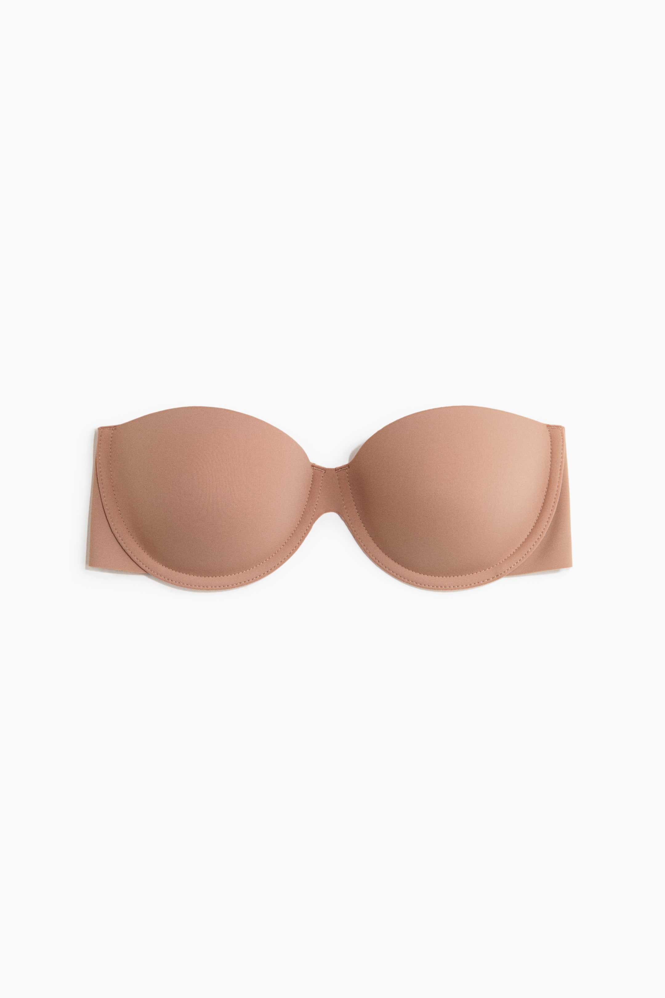 View larger image: A beige self-adhesive bra is showcased front-facing, highlighting smooth, lightly padded cups with visible stitching along the edges, and featuring no shoulder straps or back.