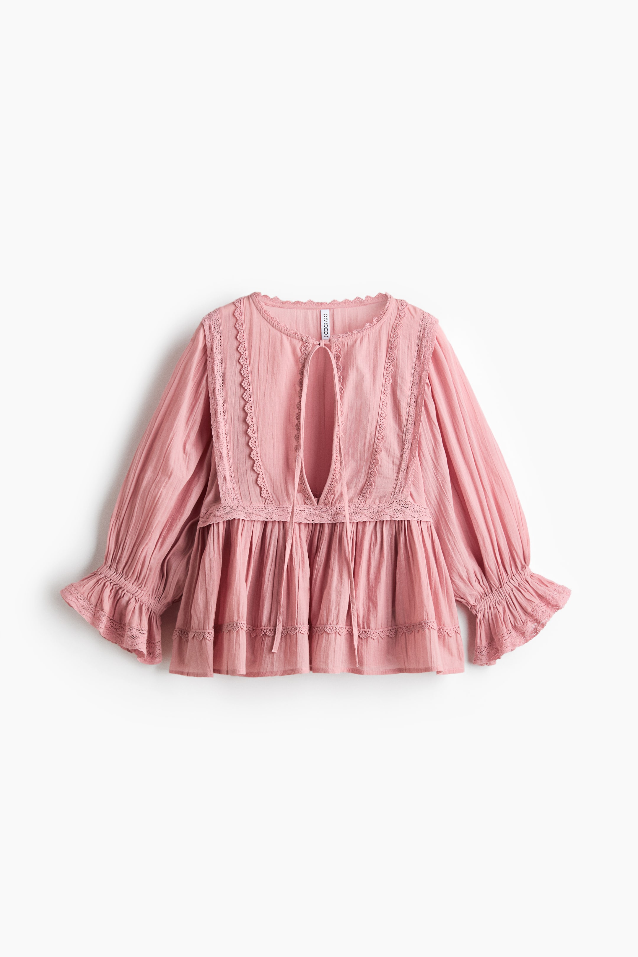 View larger image: This pink blouse presents its FRONT, crafted from an airy cotton weave. It features a round neckline and a deep V-shaped opening with narrow ties, both detailed with picot trim, along with long balloon sleeves that finish with narrow elastication at the wrists and lace-trimmed, flared cuffs. A lace-trimmed, gathered seam defines the waist and leads to a flared peplum.