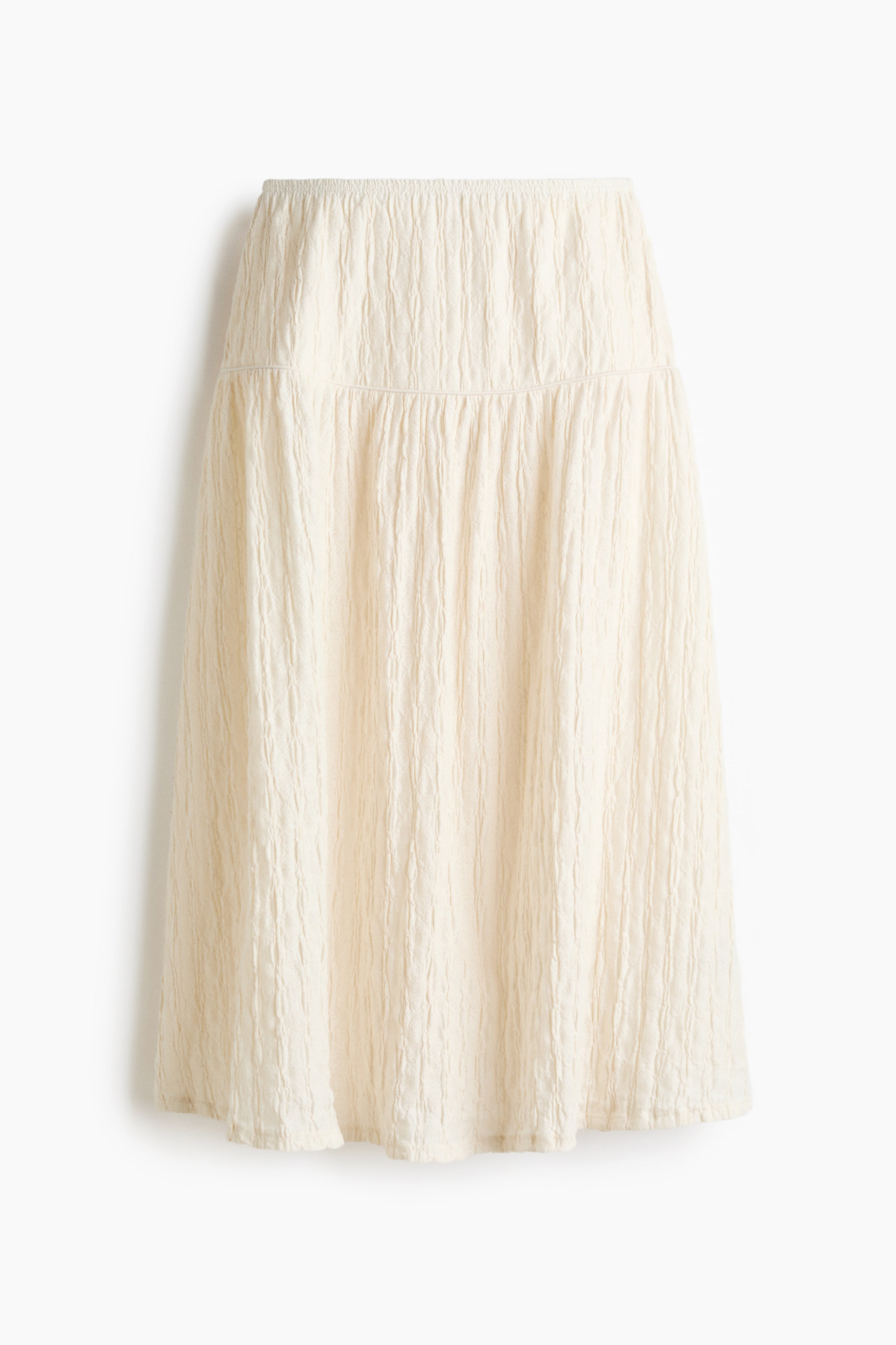 View larger image: Presenting a cream-coloured skirt FRONT, crafted from textured, crinkled fabric throughout. It features a shirred elastic waistband and a tiered design with a seam below the waist, flowing into an A-line silhouette.