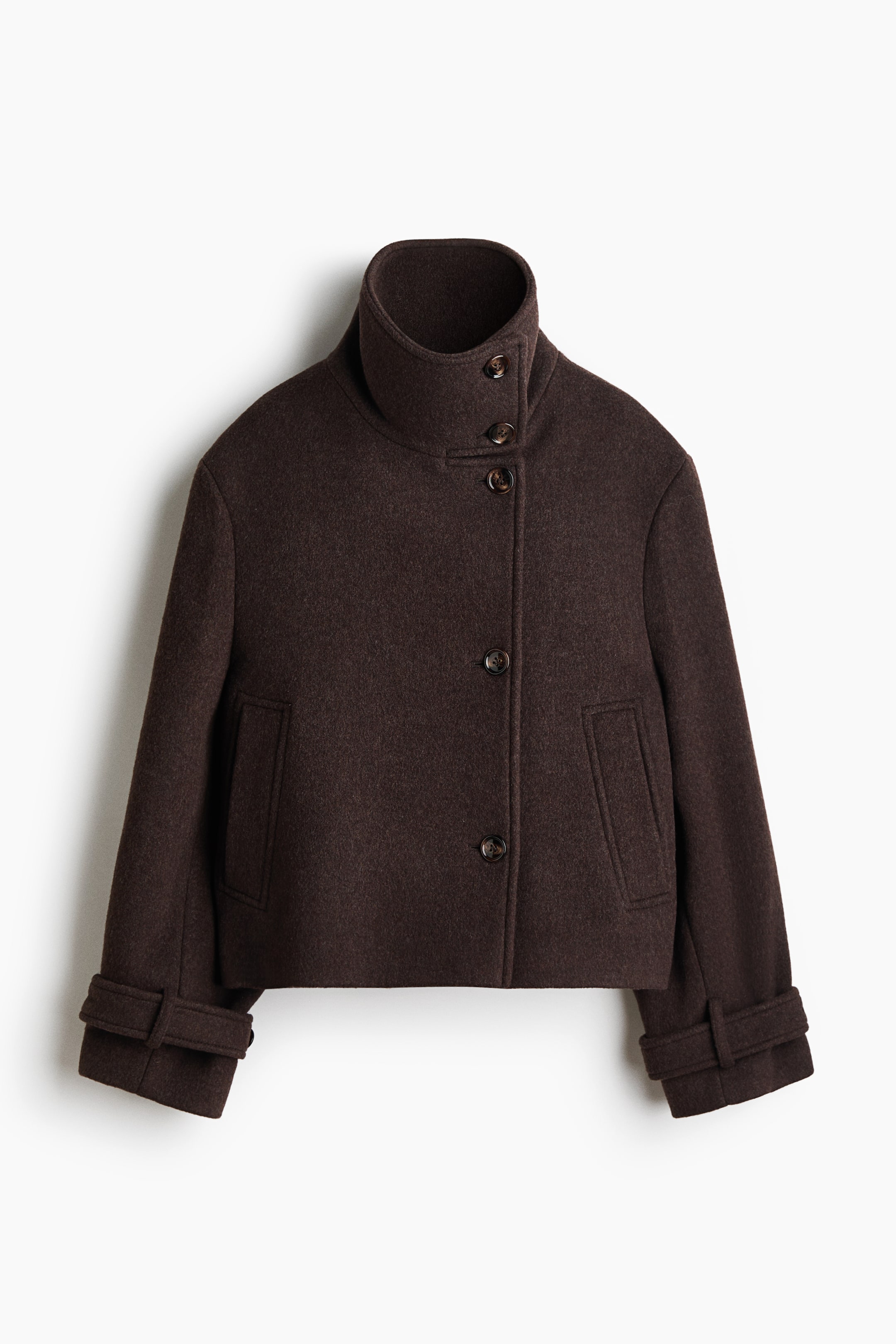 View larger image: A dark brown wool jacket is shown from the front, showcasing a cropped, boxy silhouette with an asymmetrical button-front closure. It features a high, buttoned stand-up collar, vertical welt pockets, and wide sleeves with buttoned cuff tabs.
