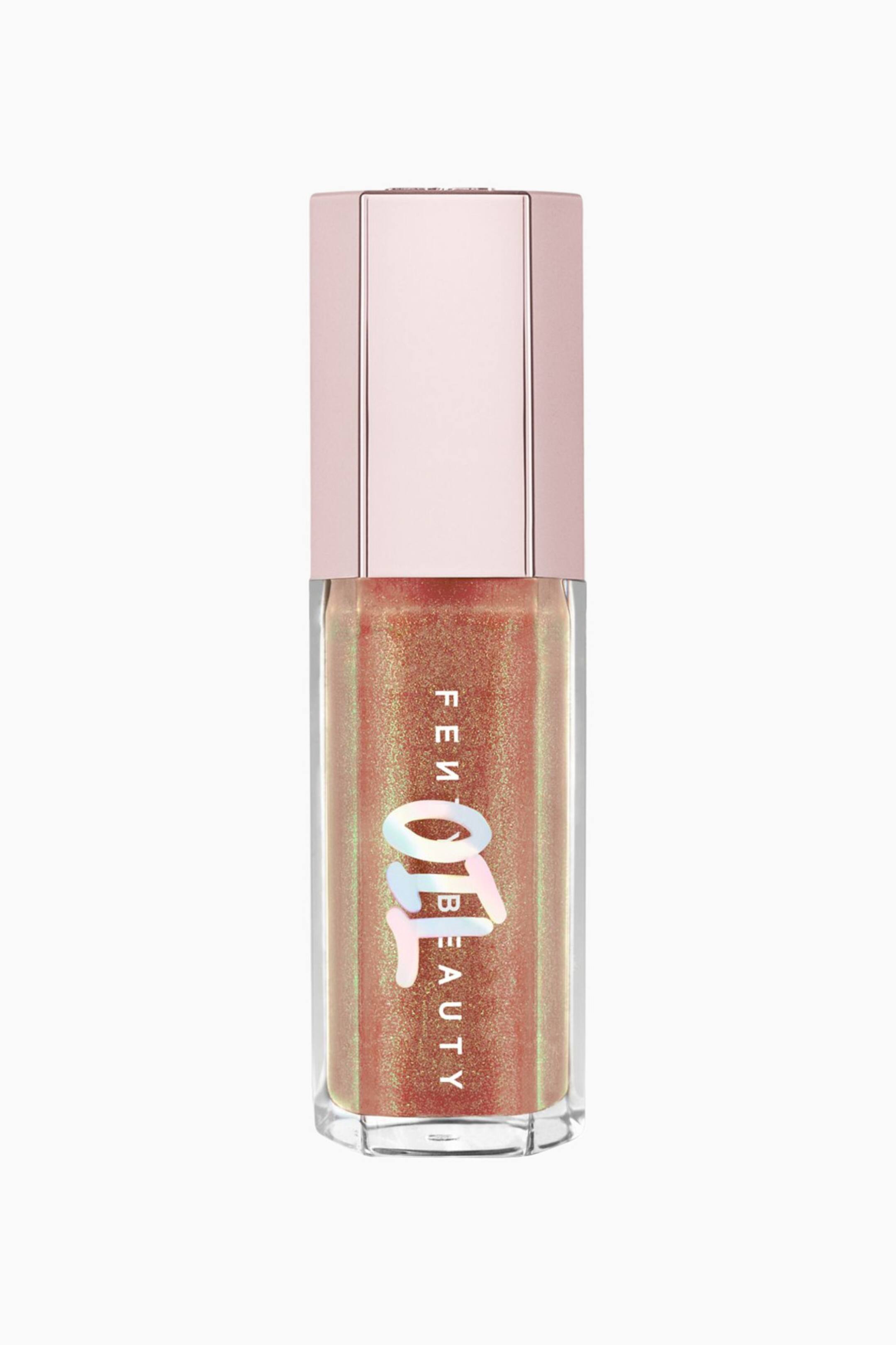 Visa större bild: Gloss Bomb Oil Luminizing Lip Oil 'n Gloss står upprätt och visar upp sin klara, hexagonala tub fylld med ett skimrande, kopparorange gloss med en grön-guldig iriserande skiftning. Produkten har en metallisk, ljusrosa hexagonformad kork och visar vit, vertikal varumärkesmärkning överlagrad med en stor, holografisk "OIL"-logotyp på framsidan.