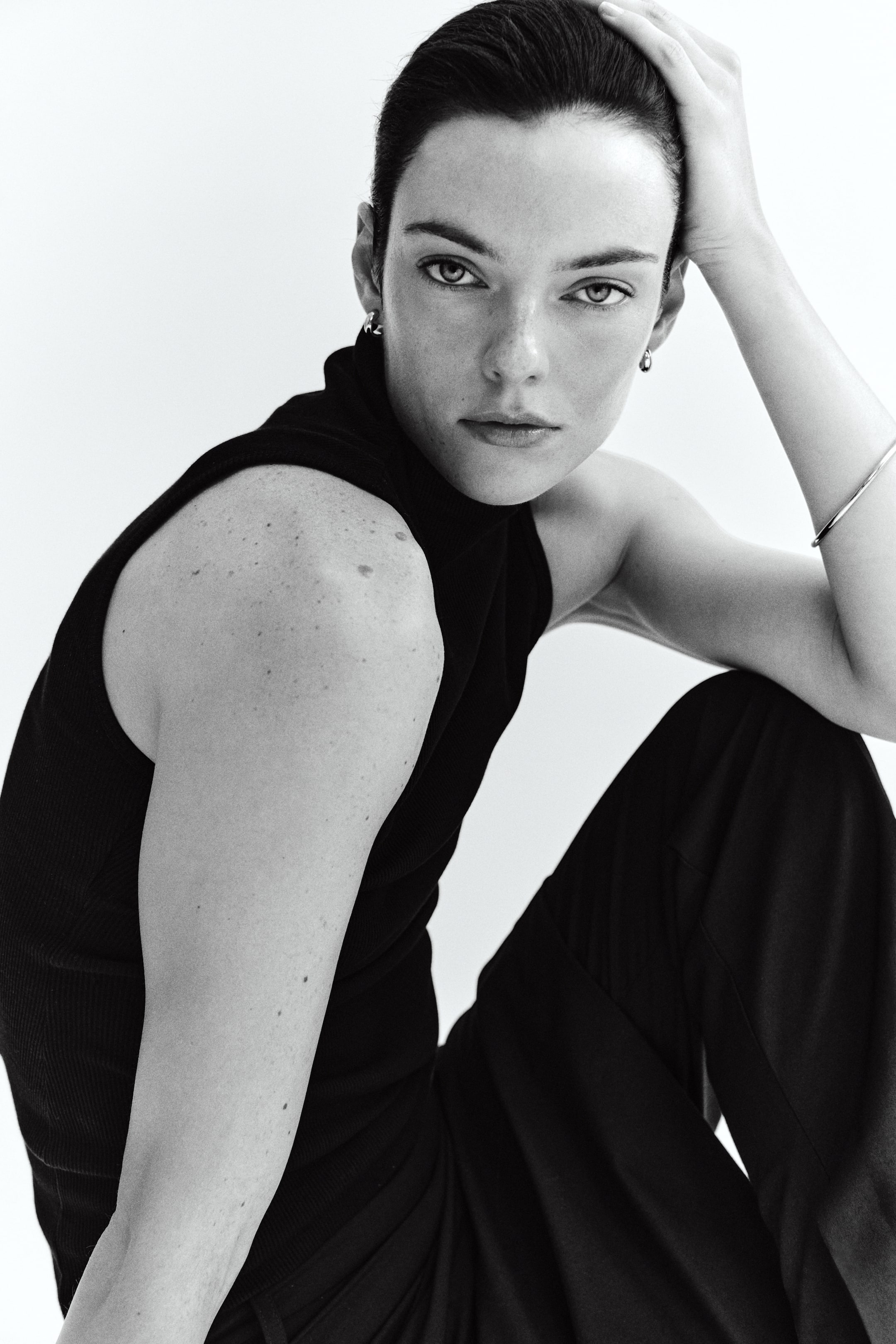 View larger image: A black, sleeveless top in ribbed jersey with a high neck is being worn by the model in a slim fit. The top is paired with dark trousers.