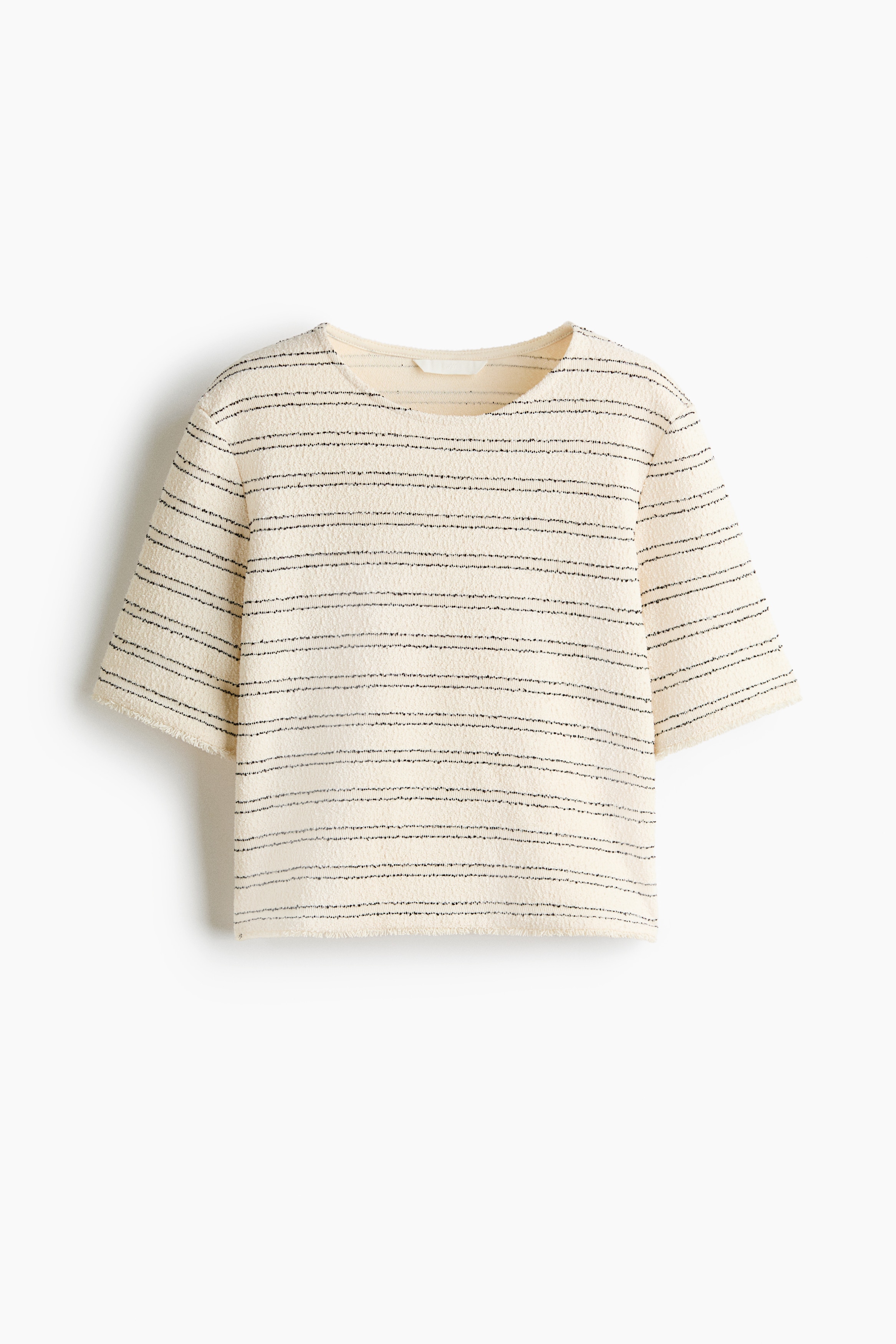 Das Model trägt ein kurzes, cremefarbenes Top im kastigen Schnitt aus strukturiertem Jersey mit schwarzen horizontalen Streifen. Das locker geschnittene Top verfügt über einen Rundhalsausschnitt, kurze Ärmel und kurze Fransenabschlüsse an den Ärmelbündchen und am Saum und wird mit Jeans in heller Waschung kombiniert.