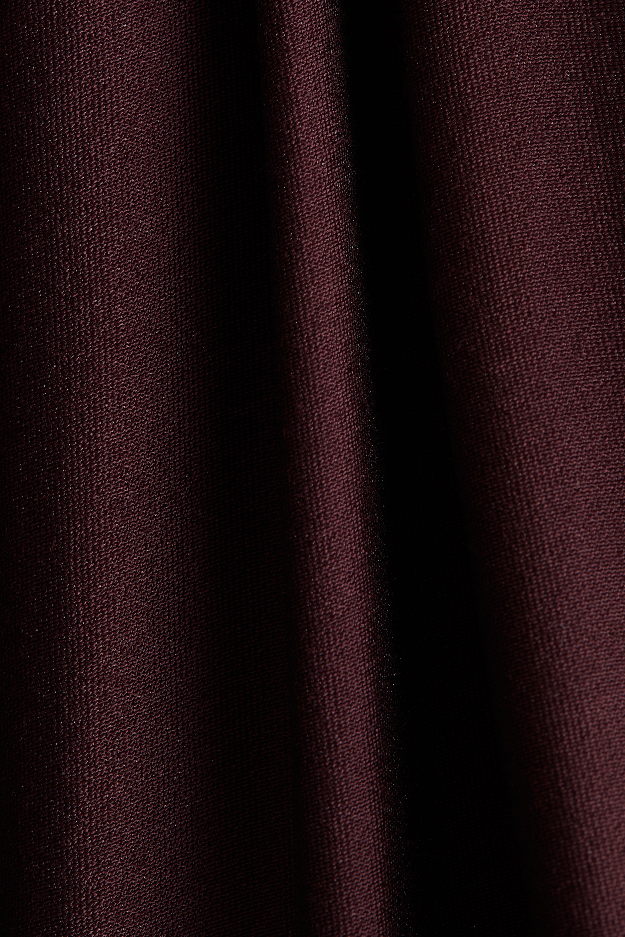View larger image: A burgundy fabric is displaying a fine, subtle weave with a slight sheen. It is draped, forming soft vertical folds and shadows.