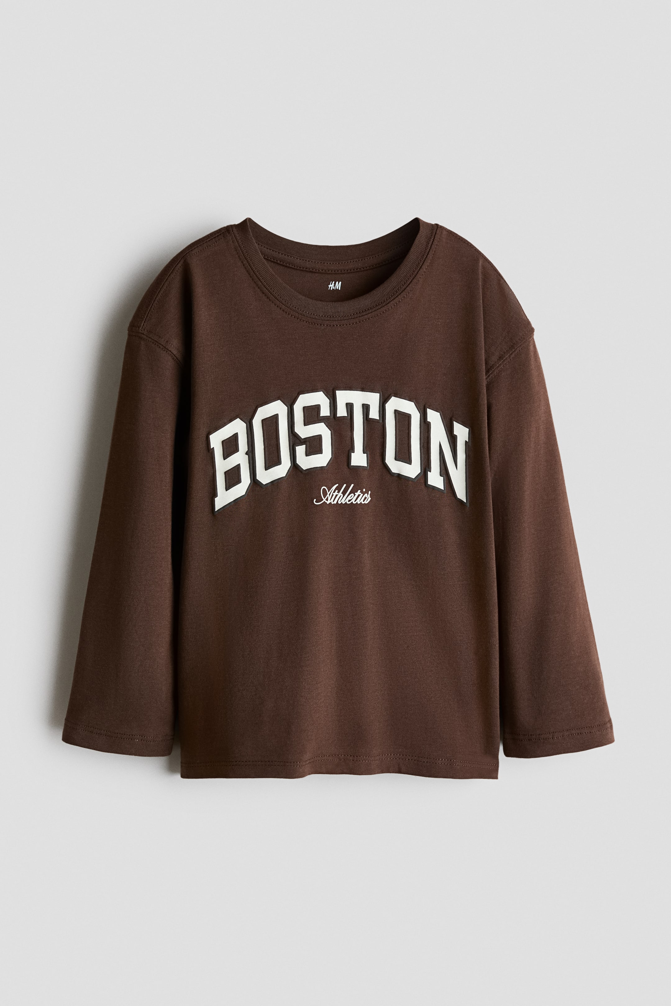 Zobacz większy obraz: Brązowy t-shirt z długim rękawem prezentuje swój przód, z prążkowanym dekoltem typu crew neck. Na koszulce widnieje napis "BOSTON" w dużych, białych, wypukłych literach aplikacji na klatce piersiowej, z "Athletics" w mniejszym, białym, haftowanym tekście pisanym poniżej.