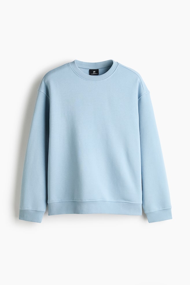 A light blue sweatshirt is hanging facing the front, showcasing a loose-fit silhouette with dropped shoulders and long sleeves. The garment features a round, rib-trimmed neckline alongside wide ribbed cuffs and a matching ribbed hem. - 1