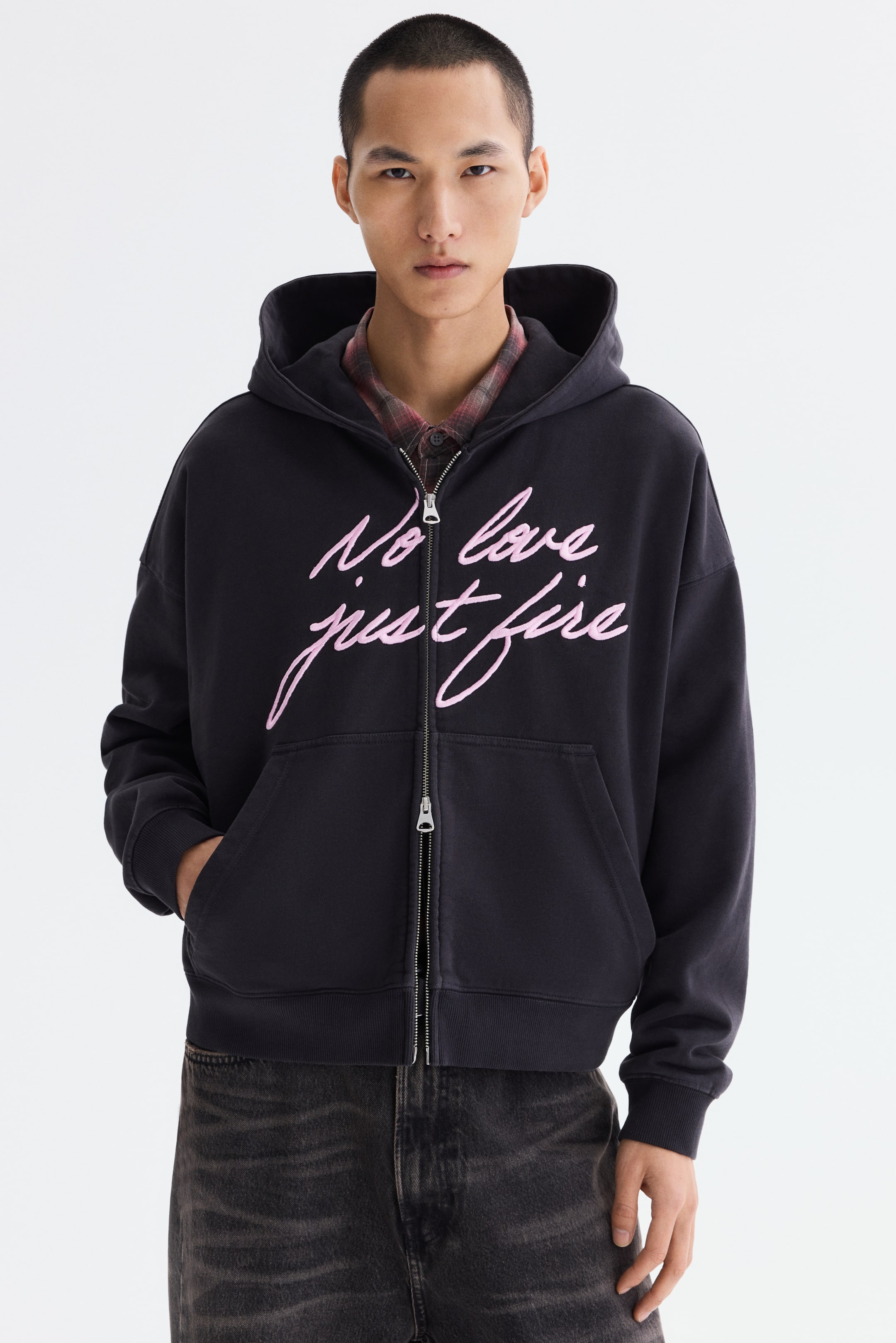 查看大圖: 一件黑色全拉鍊連帽外套，胸前飾有粉色手寫體字樣「No love just fire」。採用銀色拉鍊、袋鼠口袋、羅紋袖口與下襬，以及連帽設計；前襟微開，內搭格紋襯衫呈現層次感。