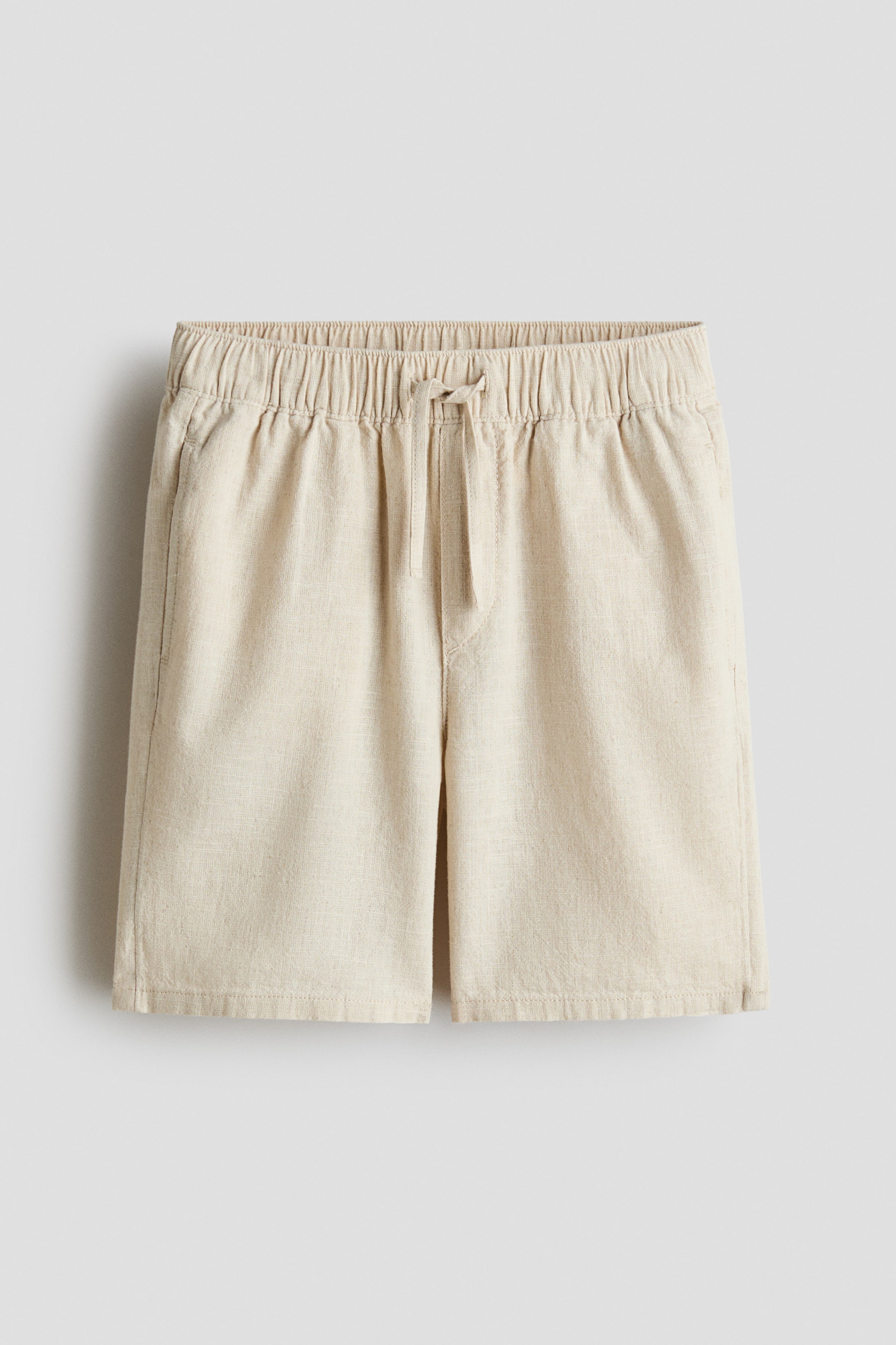View larger image: Light beige textured shorts feature an elasticated waistband with a drawstring tied at the front and visible side pockets.