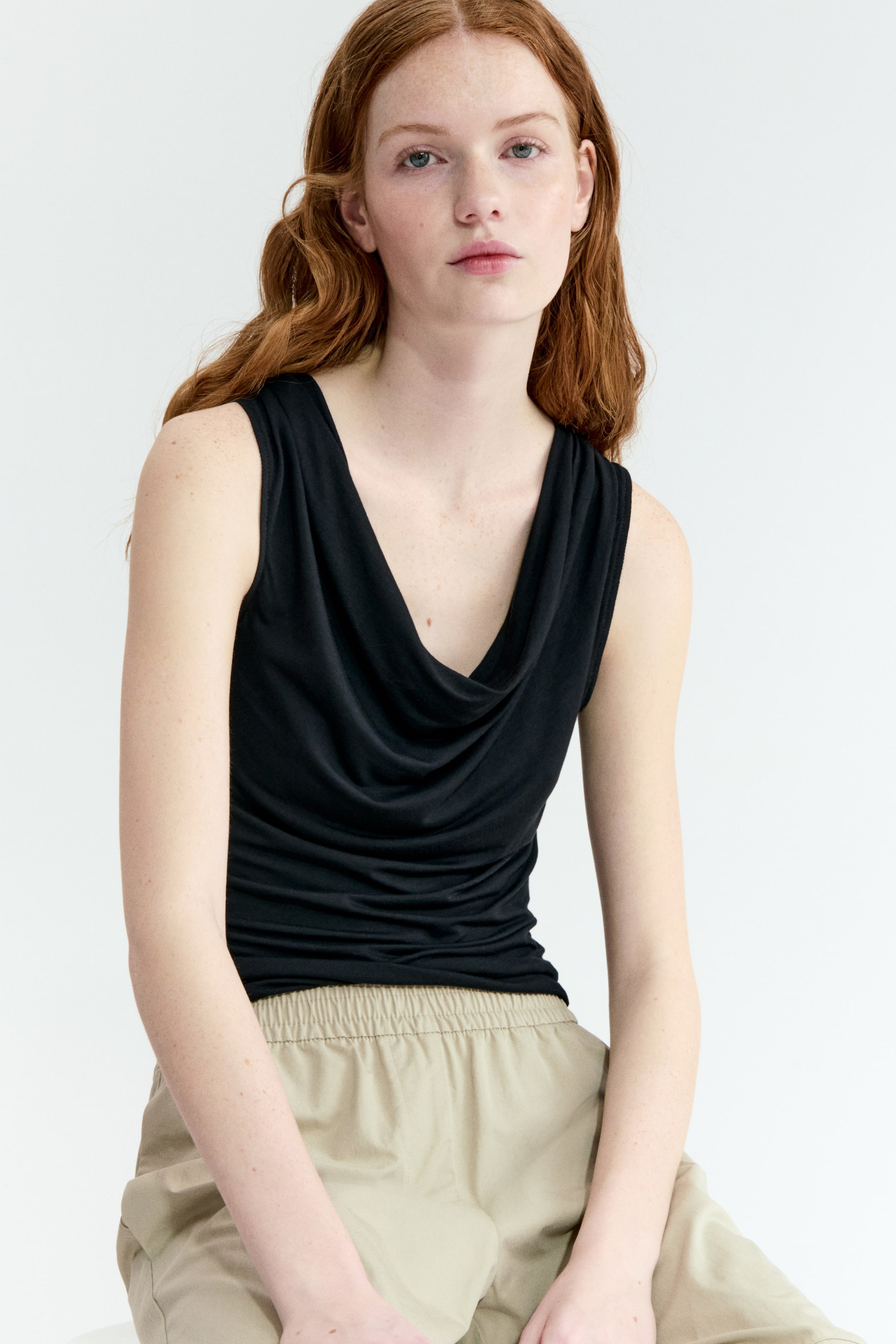 Xem ảnh lớn hơn: Áo đen không tay với cổ áo draped cowl và thân áo ôm sát.