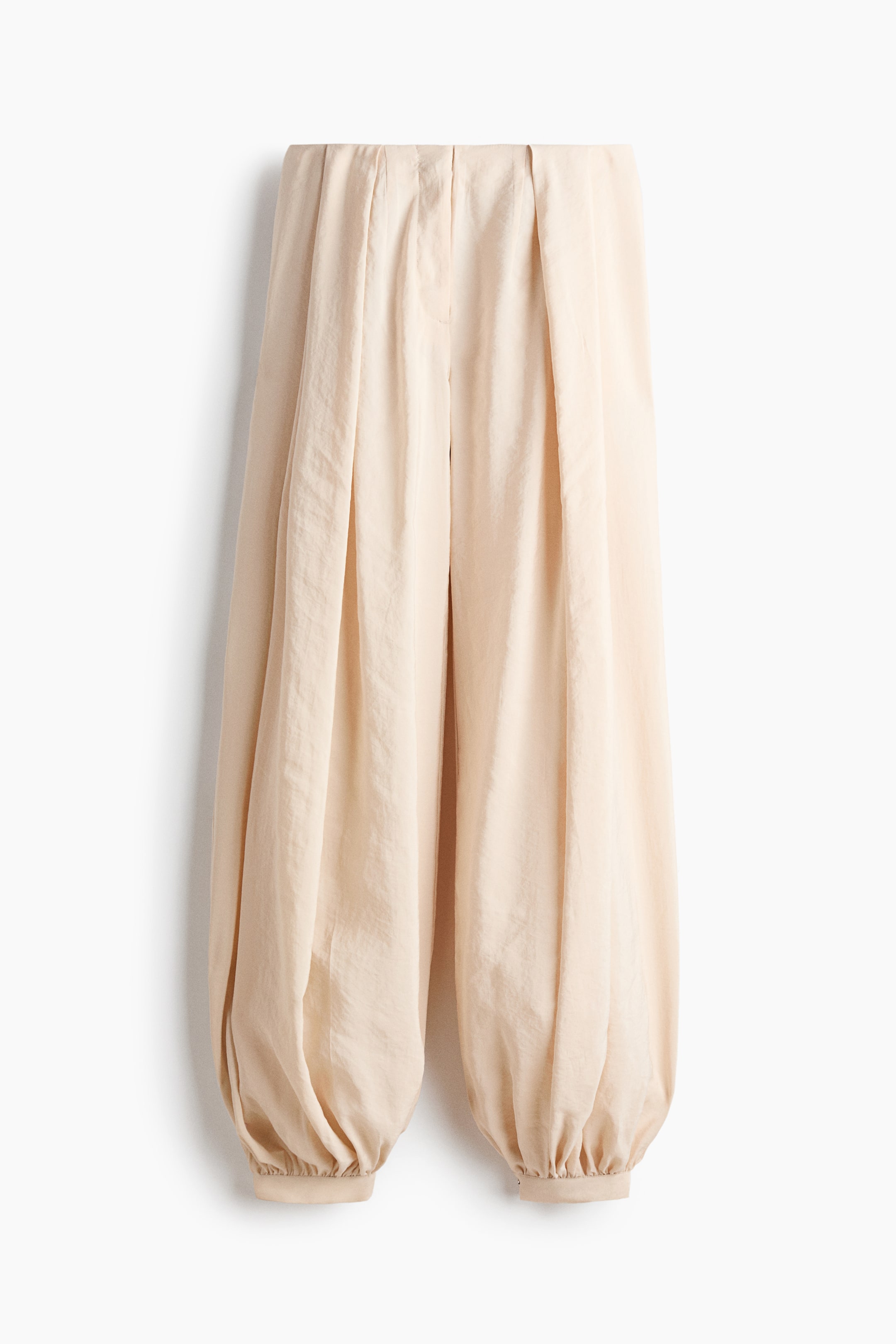 View larger image: Presenting a pair of light beige, high-waisted trousers with a frontal view. These trousers showcase distinct pleats, wide voluminous legs, and elasticized cuffs, creating a balloon-like silhouette.
