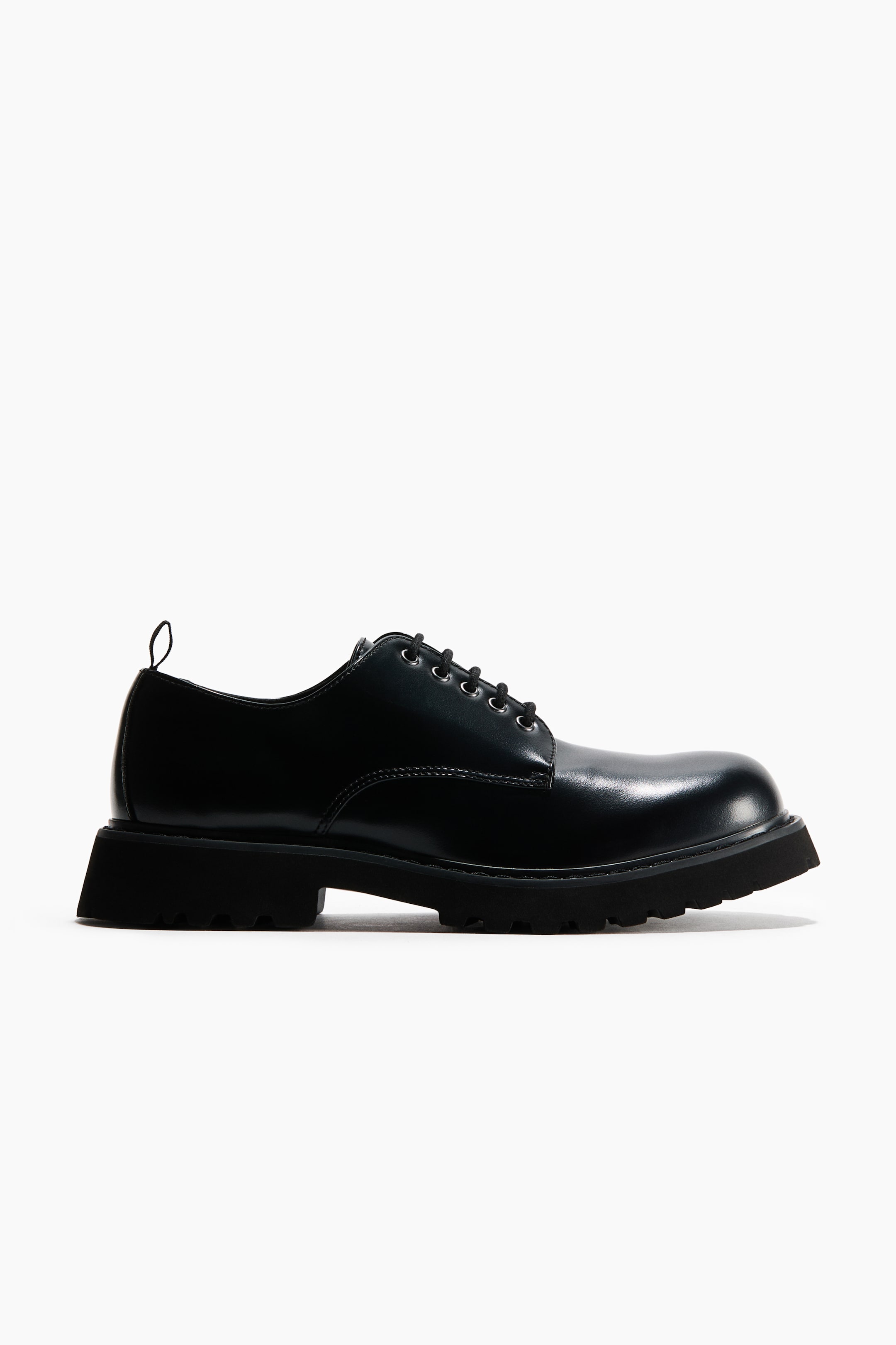 View larger image: A black polished leather derby shoe featuring black laces threaded through metal eyelets, displaying a thick, lugged black sole with a squared-off heel and a small pull tab at the back, angled to the front.